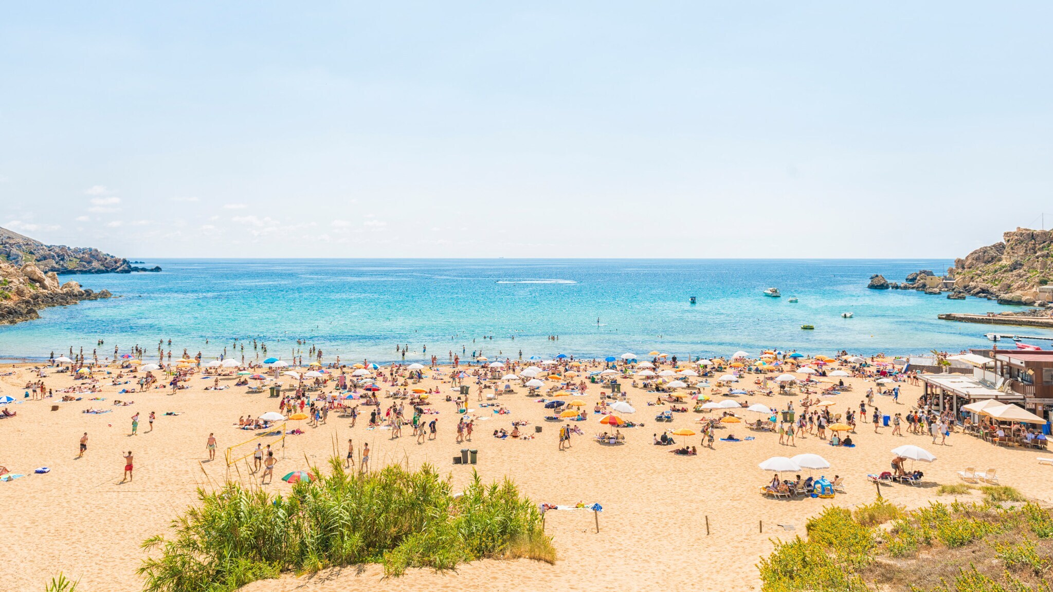 Strand mit vielen Menschen, Sonnenschirmen und klarem blauem Meer unter hellem Himmel