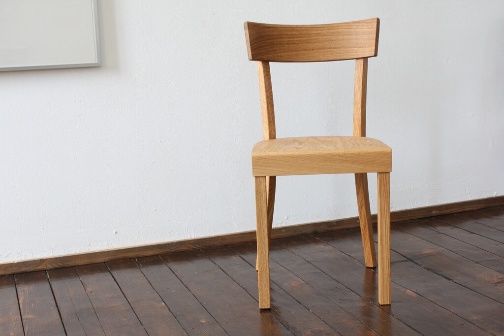 Ein brauner Holzstuhl steht auf Holzdielen vor einer weißen Wand