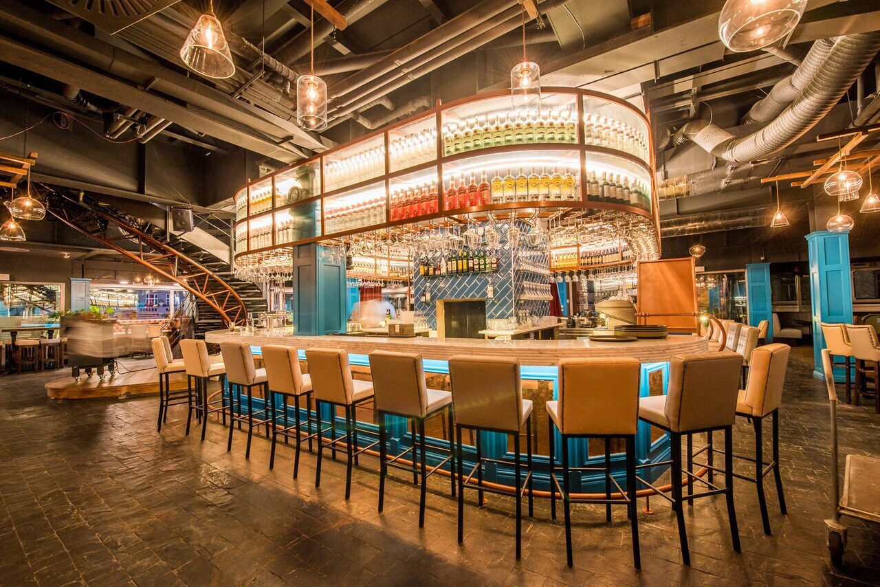 Eine ovale, beleuchtete Bar mit Stühlen drumherum in einem industriellen Ambiente