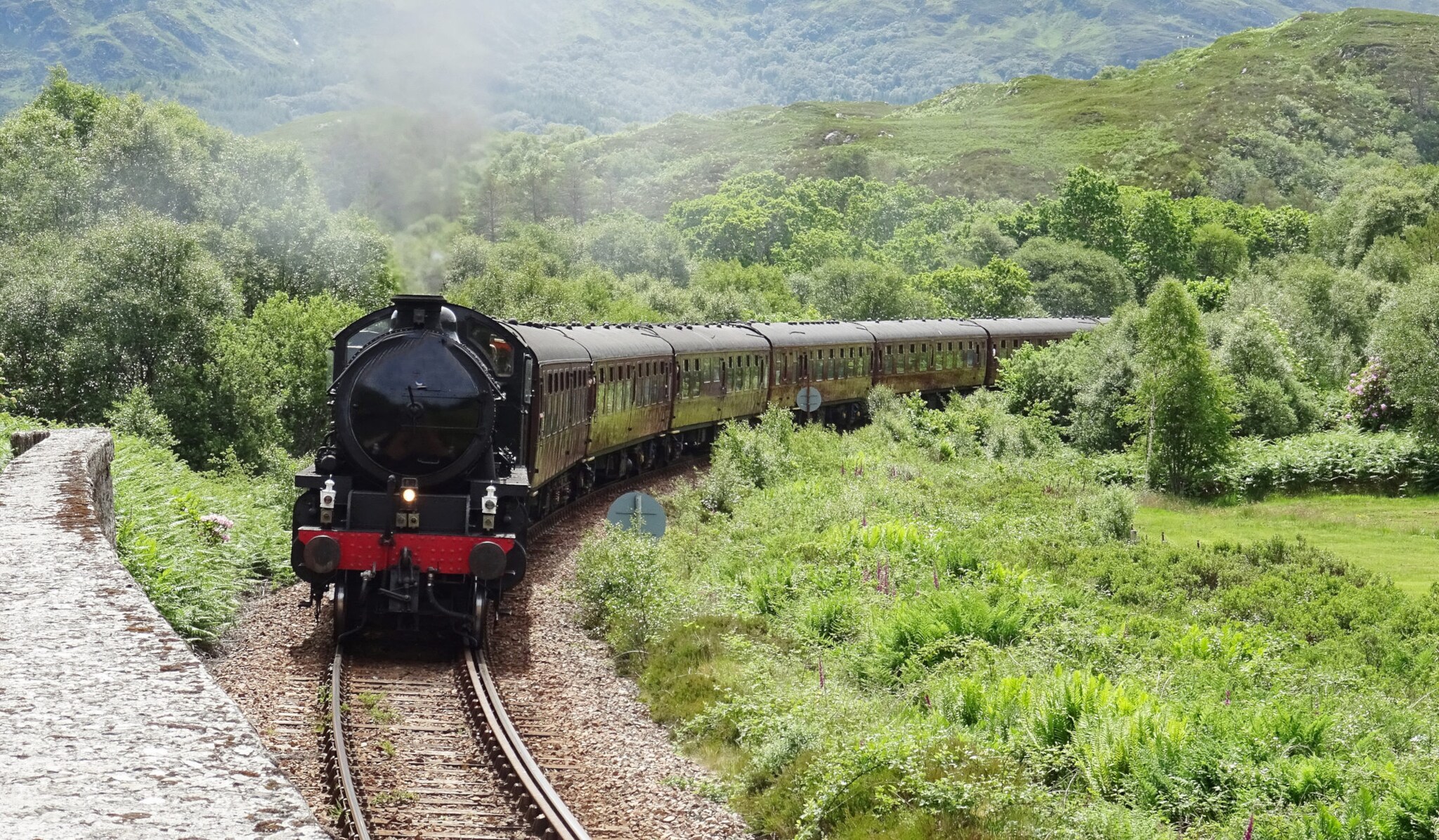 Der historische Jacobite Steam Train fährt durch grüne Landschaft in Schottland. Der historische Jacobite Steam Train fährt durch grüne Landschaft in Schottland.