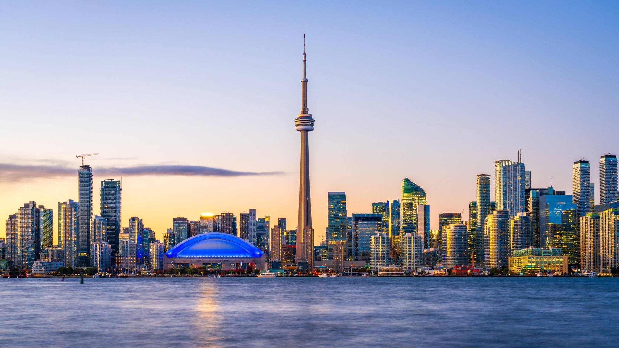 Skyline von Toronto mit Hochhäusern und Fernsehturm am Wasser im Abendlicht.