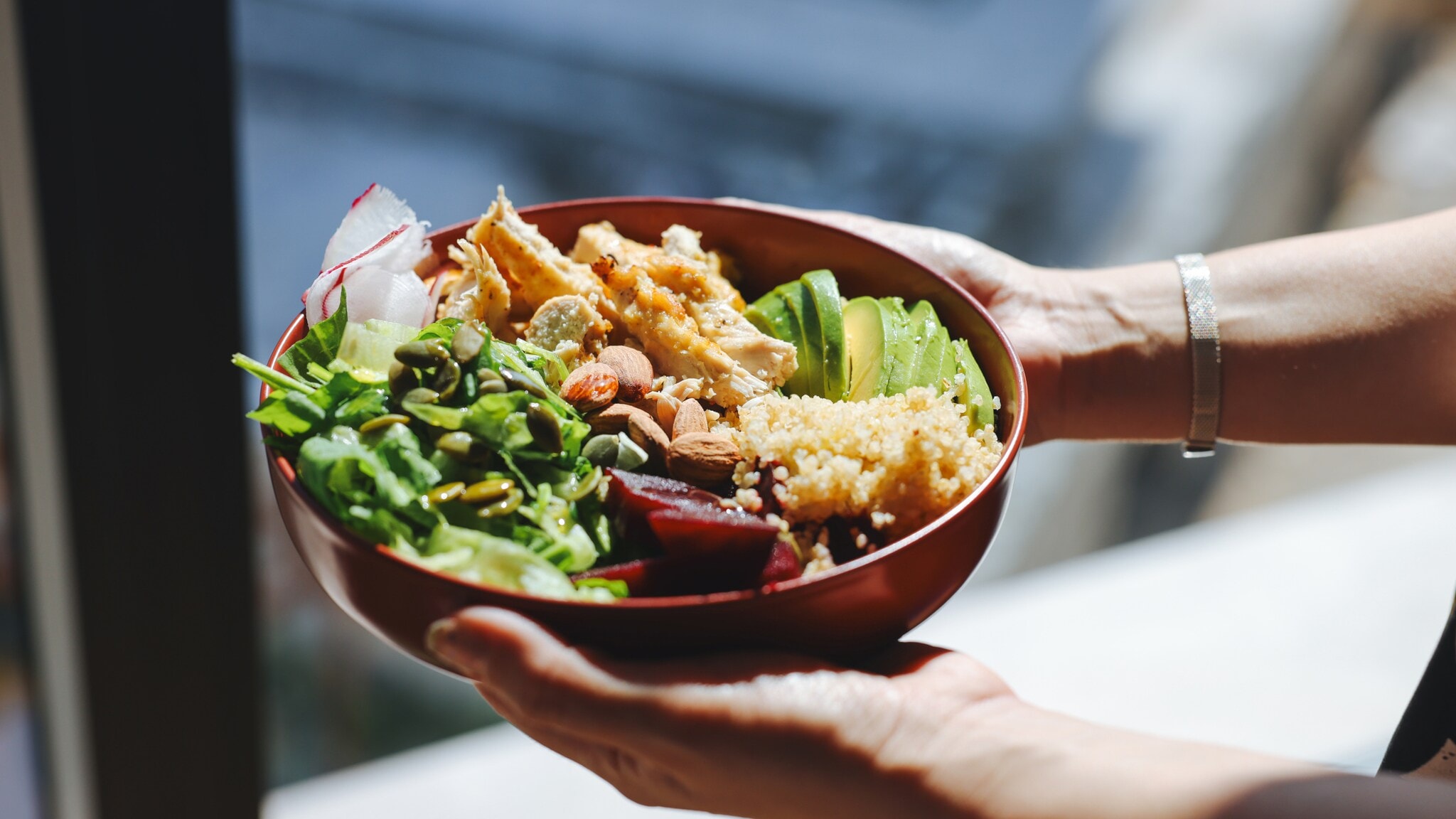 Schale mit gemischtem Salat, Avocadoscheiben, Quinoa, Nüssen und gebratenem Hähnchen, gehalten von zwei Händen. Schale mit gemischtem Salat, Avocadoscheiben, Quinoa, Nüssen und gebratenem Hähnchen, gehalten von zwei Händen.