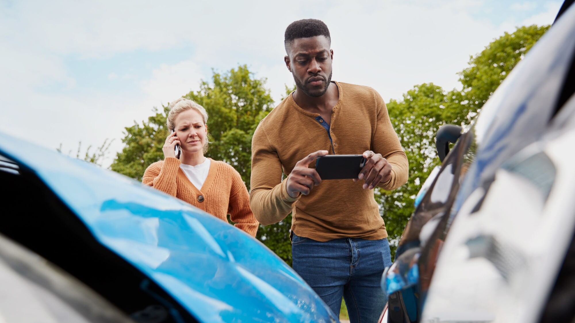 Ein Mann und einer Frau mit Smartphones stehen hinter zwei Autos mit Blechschäden, er macht ein Foto vom Schaden. Ein Mann und einer Frau mit Smartphones stehen hinter zwei Autos mit Blechschäden, er macht ein Foto vom Schaden.