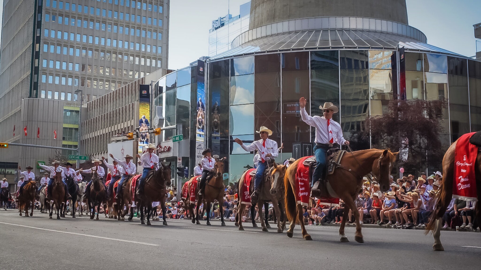 Cowboys auf Pferden winken ins Publikum während einer Parade auf einer Straße im Stadtzentrum. Cowboys auf Pferden winken ins Publikum während einer Parade auf einer Straße im Stadtzentrum.
