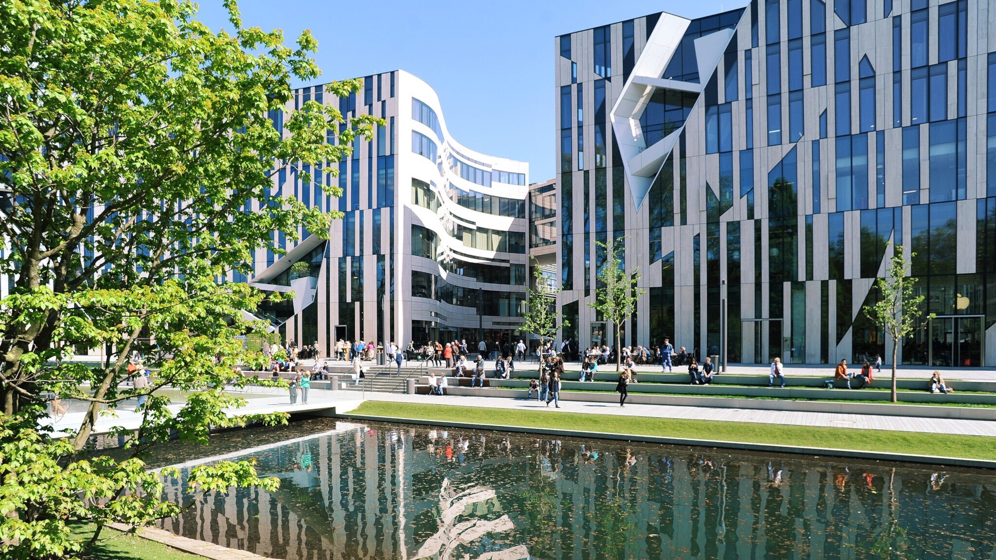 Moderne Bürogebäude mit Glasfassaden am Wasserbecken im Kö-Bogen Düsseldorf, Menschen sitzen und gehen auf der Promenade