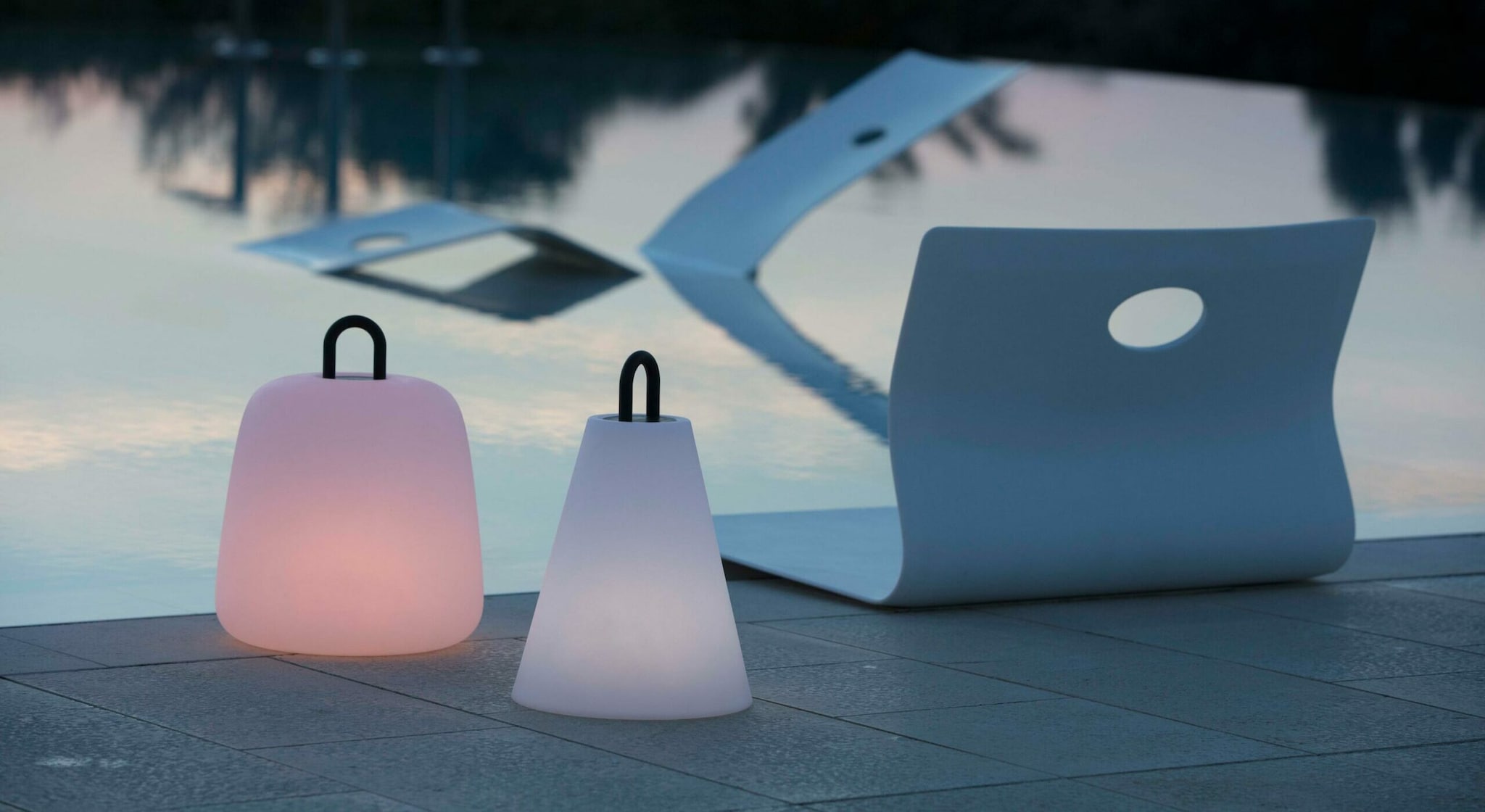 Zwei portable Leuchten stehen vor einem Pool im Freien.