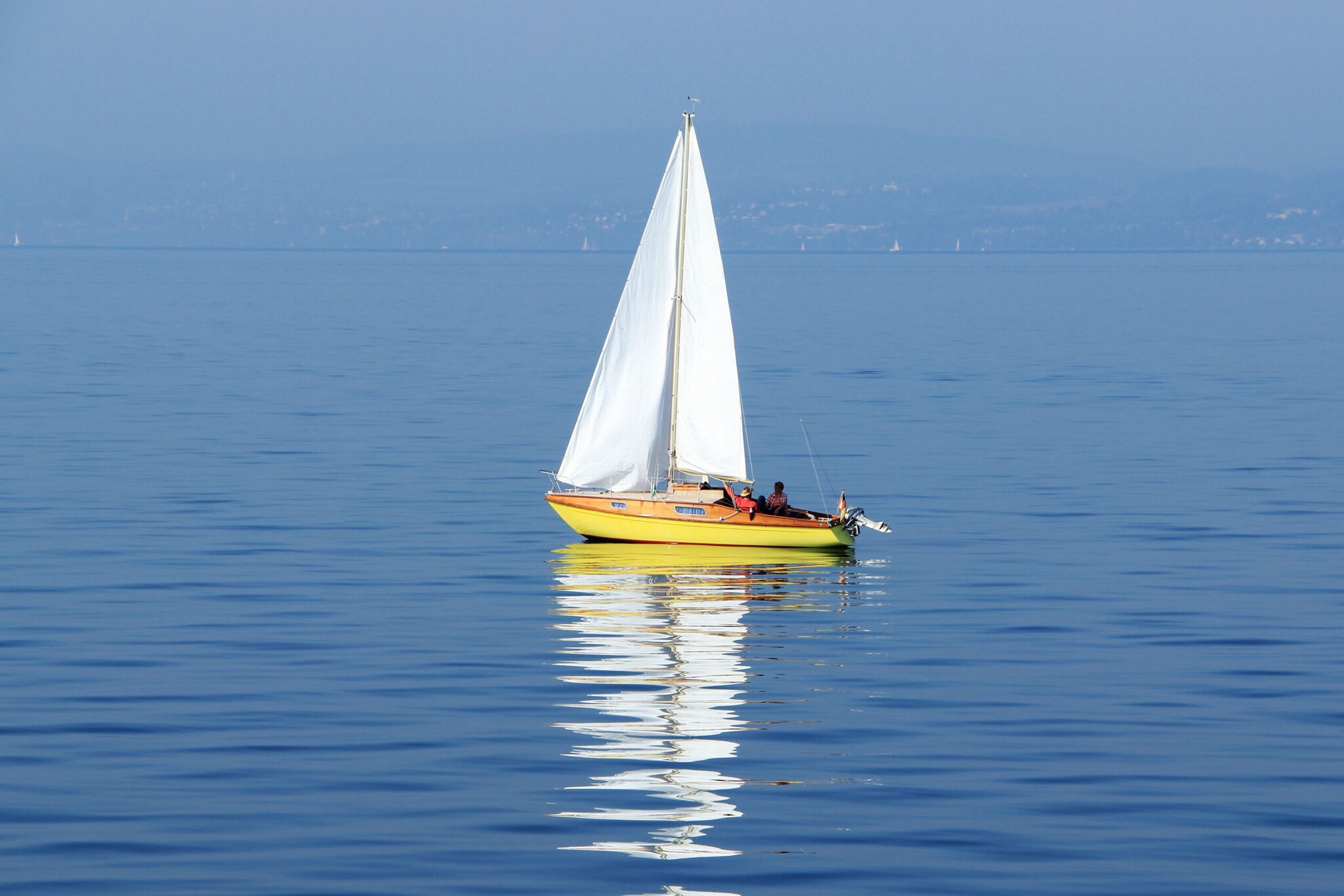 Eine kleine Jacht mit mehreren Personen an Bord vor einer Küste Eine kleine Jacht mit mehreren Personen an Bord vor einer Küste