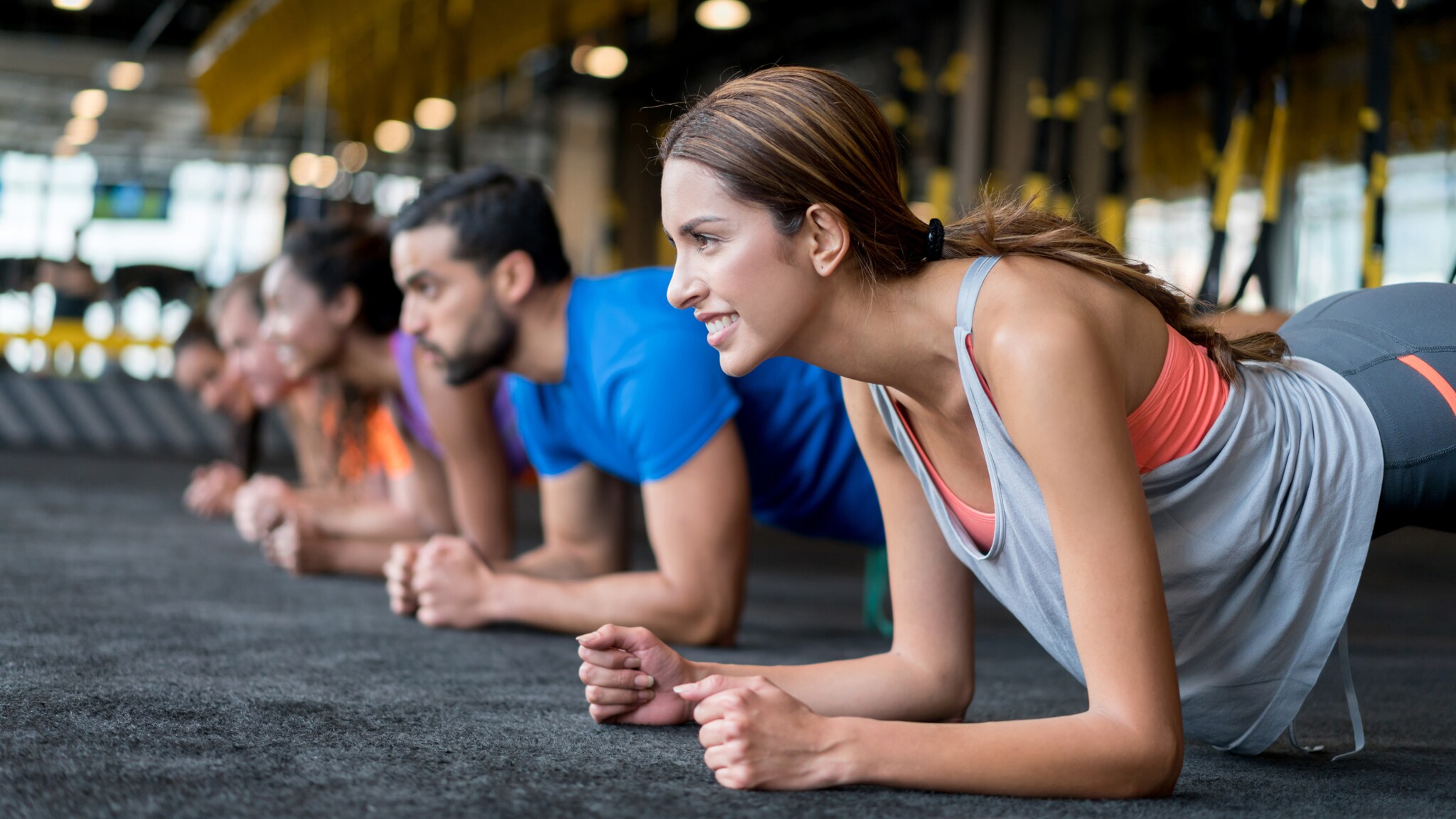 Gruppe von Menschen in Sportkleidung macht Plank-Übung auf Boden in Fitnessstudio.