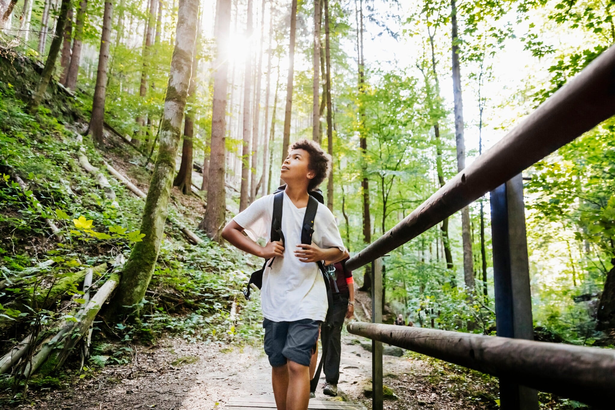 Ein Junge mit Rucksack läuft staunend und nach oben blickend durch einen Wald. Ein Junge mit Rucksack läuft staunend und nach oben blickend durch einen Wald.