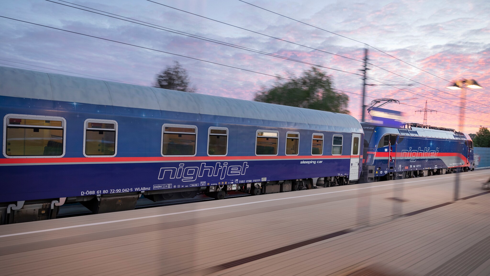 Nightjet-Schlafwagen und Lokomotive auf einem Bahnhof bei Sonnenuntergang. Nightjet-Schlafwagen und Lokomotive auf einem Bahnhof bei Sonnenuntergang.