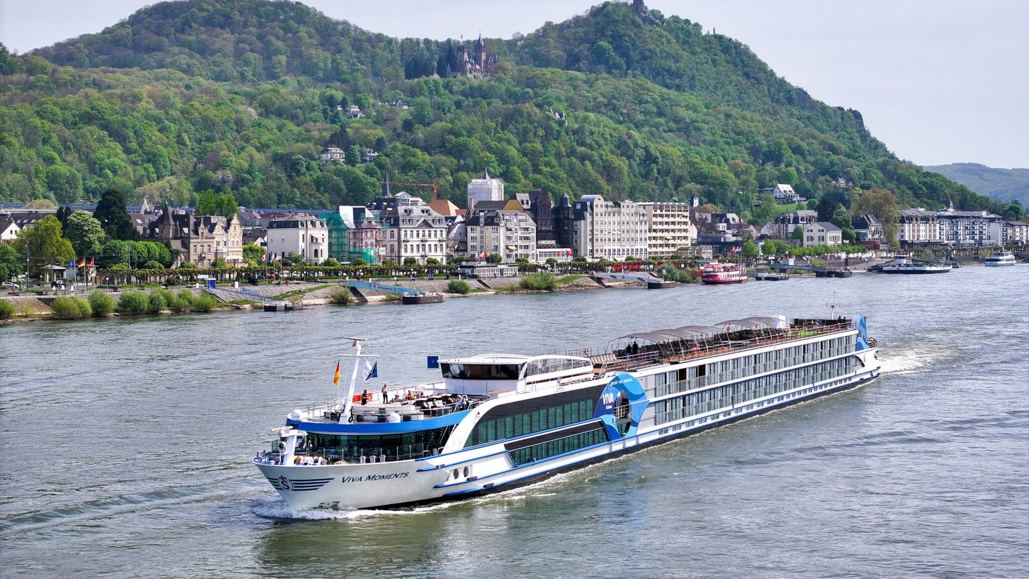 Flusskreuzfahrtschiff Viva Moments fährt vorbei an Kleinstadt am Ufer vor grüner Hügellandschaft mit Burg. Flusskreuzfahrtschiff Viva Moments fährt vorbei an Kleinstadt am Ufer vor grüner Hügellandschaft mit Burg.