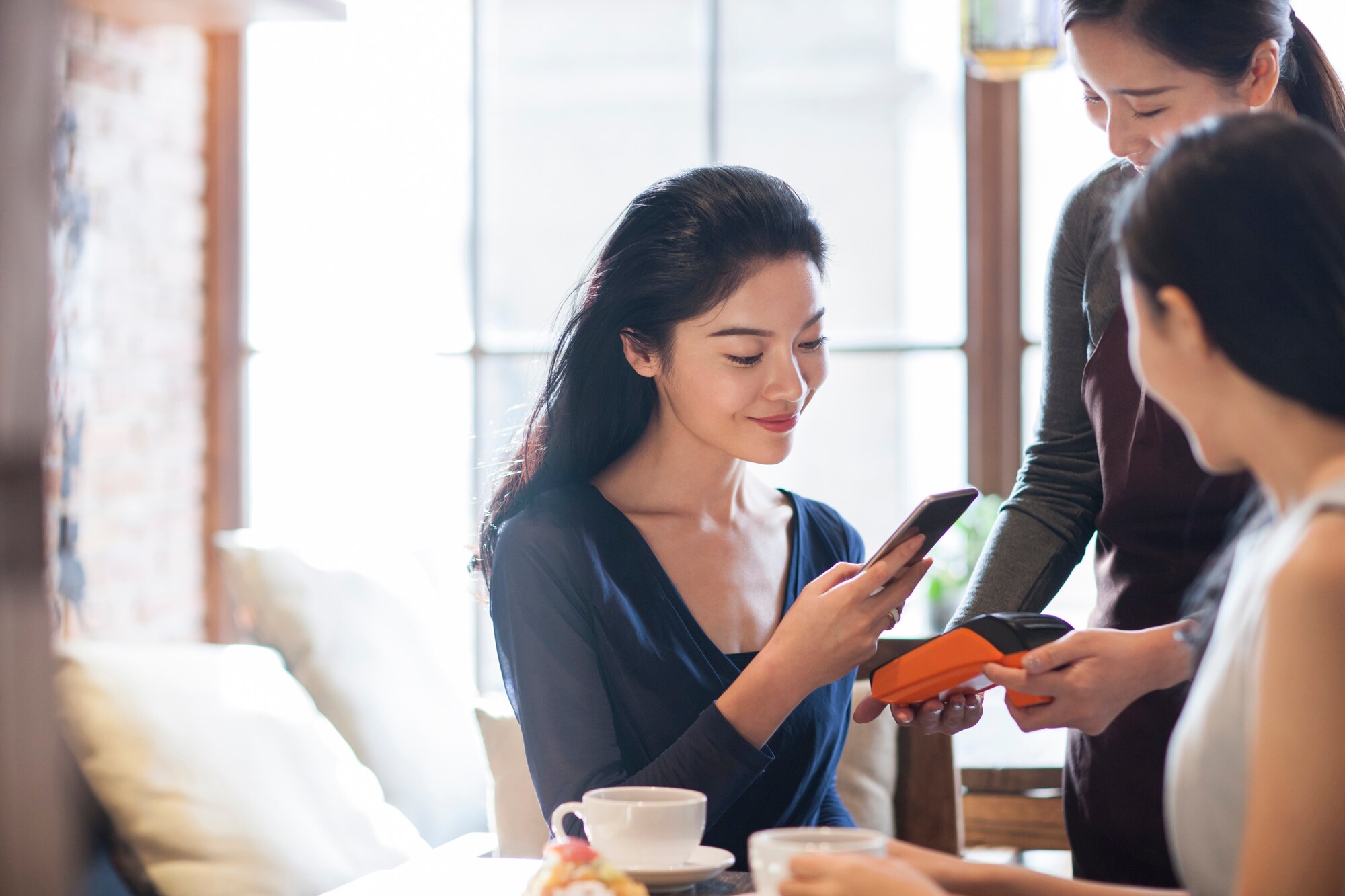 Eine junge Frau bezahlt kontaktlos mit ihrem Smartphone via Apple Pay in einem Café