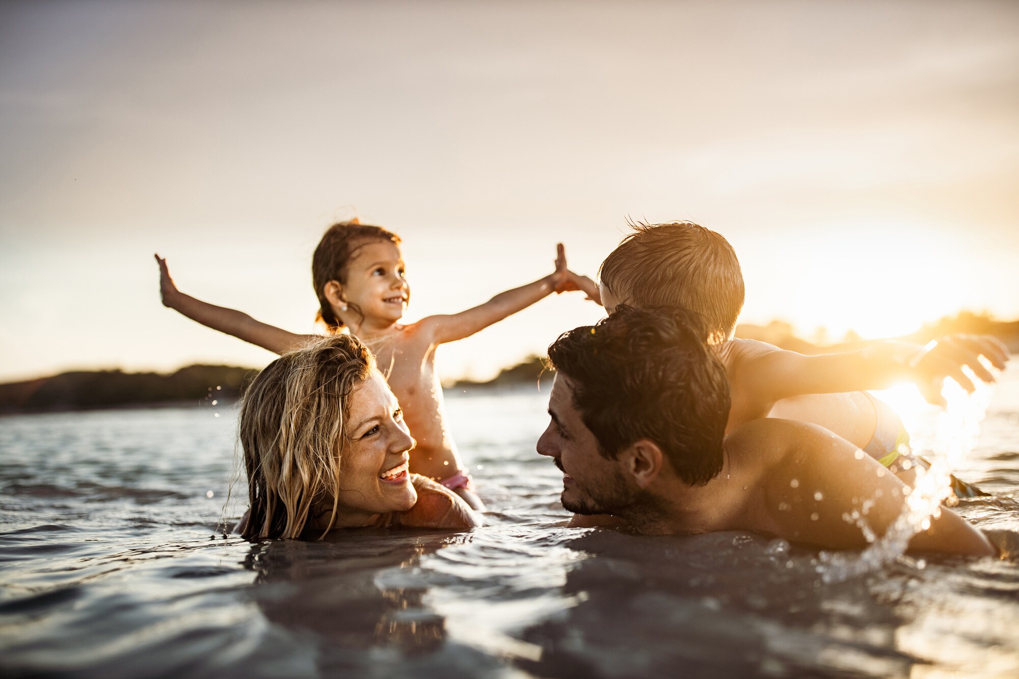 Eine junge, glückliche Familie mit zwei Kindern badet im Meer bei Sonnenuntergang