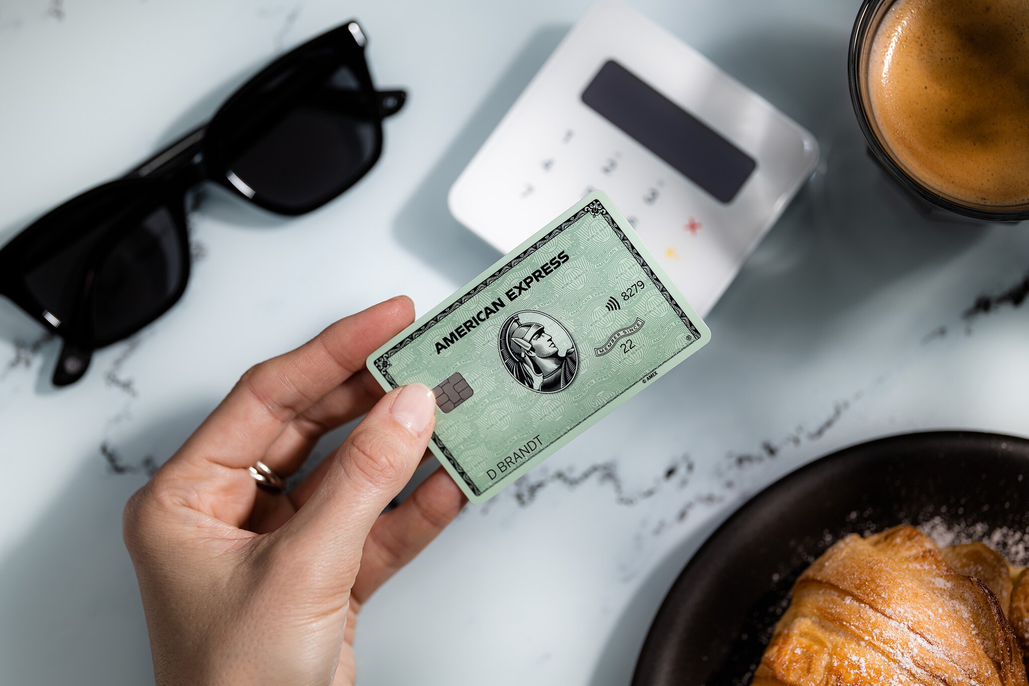 Kontaktlose Zahlung an einem Kartenlesegerät in einem Café mit einer grünen American Express Card