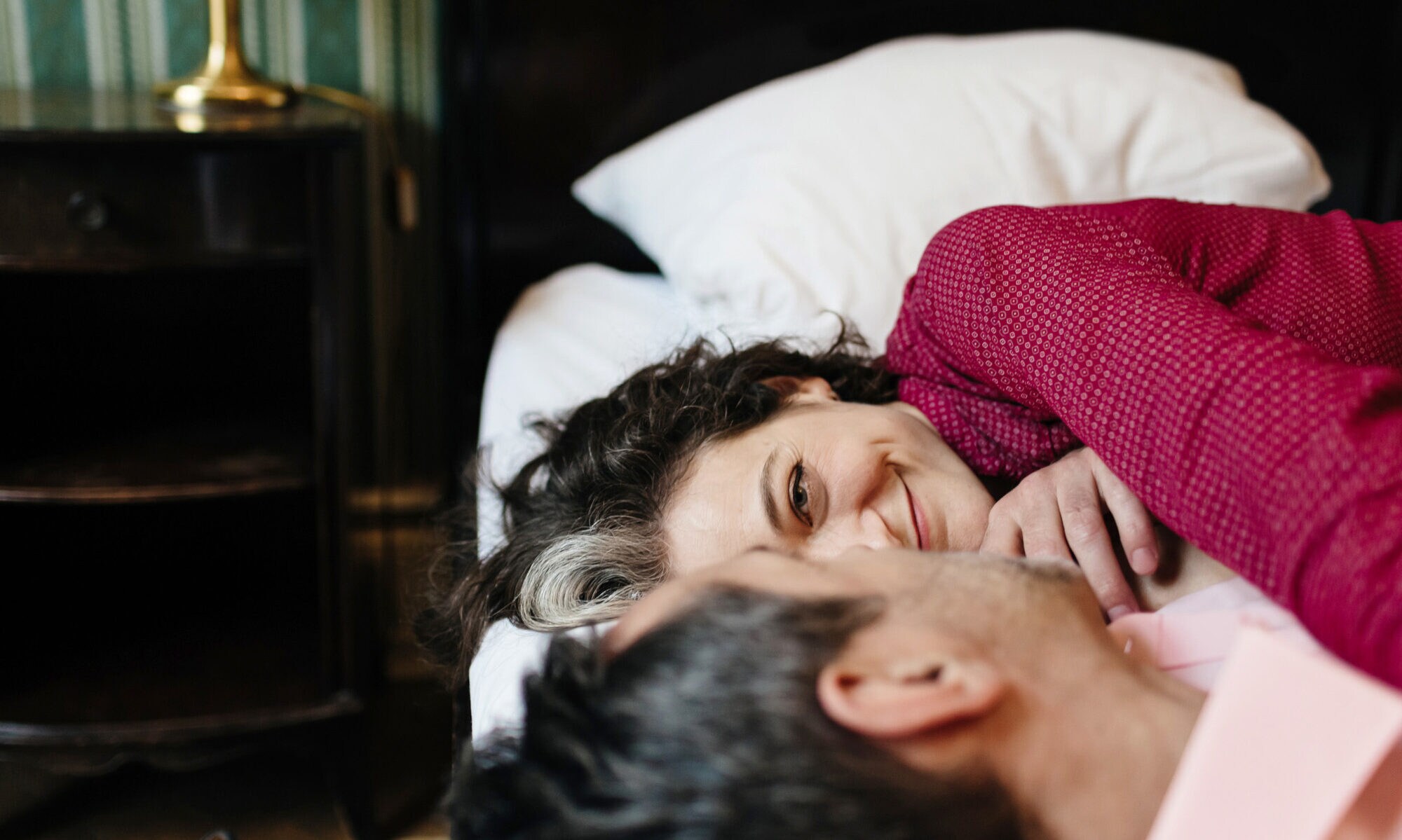 Nahaufnahme von den Köpfen eines Paares, das in einem Hotelbett liegt und sich zufrieden lächelnd anschaut