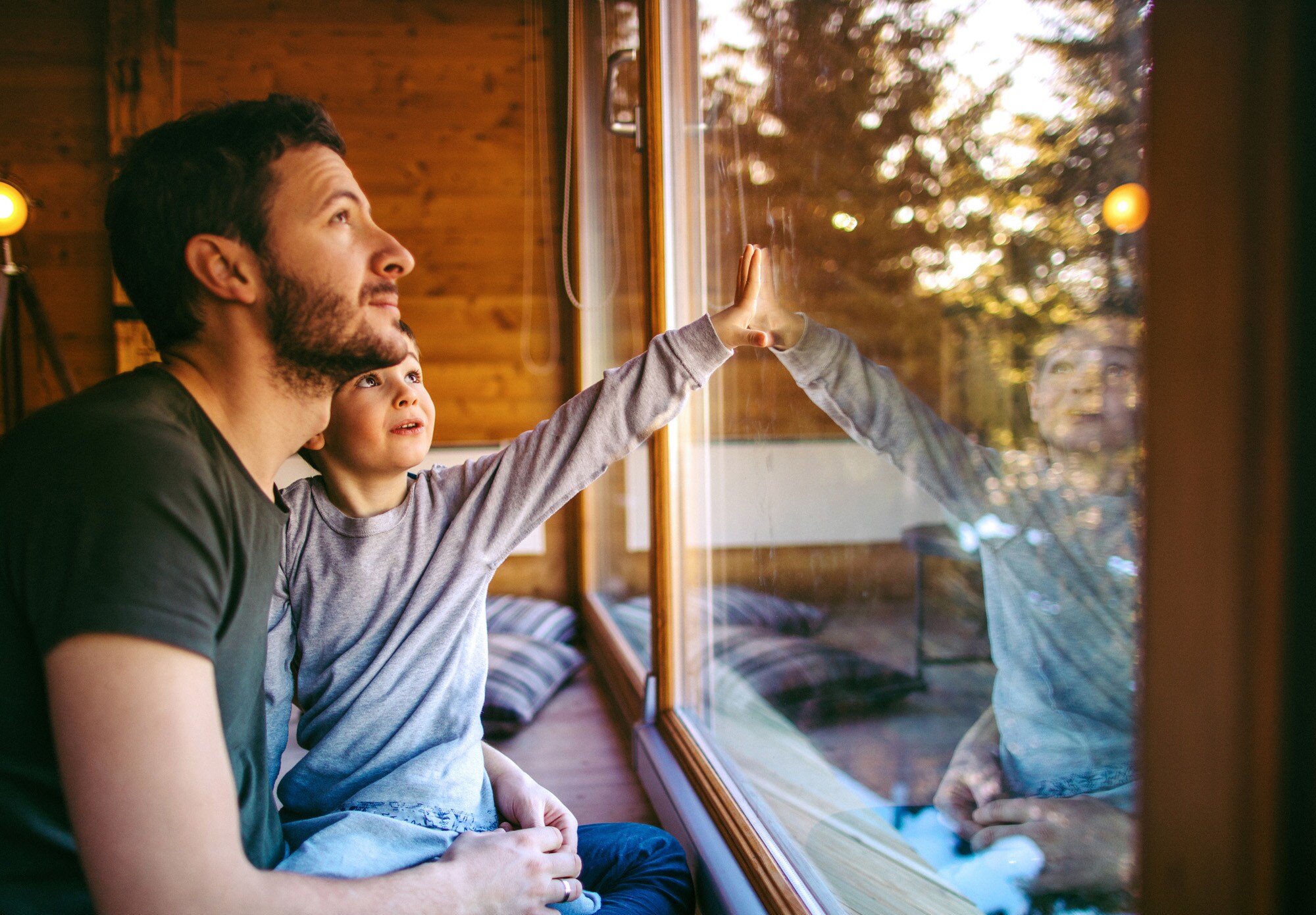 Schutz für die Liebsten: Die inkludierte Versicherung deiner Amex greift auch bei deinen Kindern. Ein Mann mit Kind auf dem Schoß blickt aus dem Fenster
