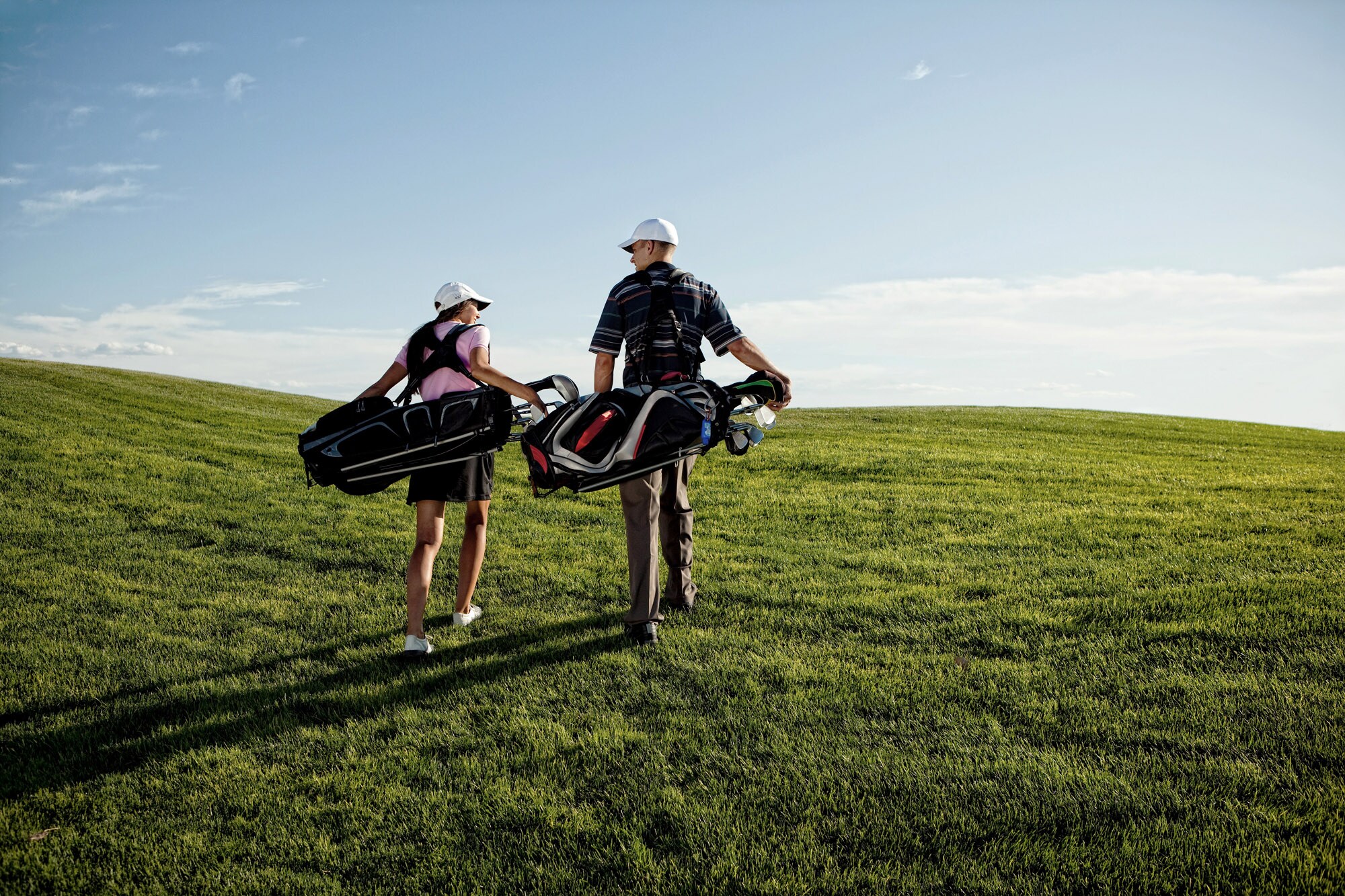 Ein Pärchen trägt sein Golfequipment über einen Golfplatz Ein Pärchen trägt sein Golfequipment über einen Golfplatz