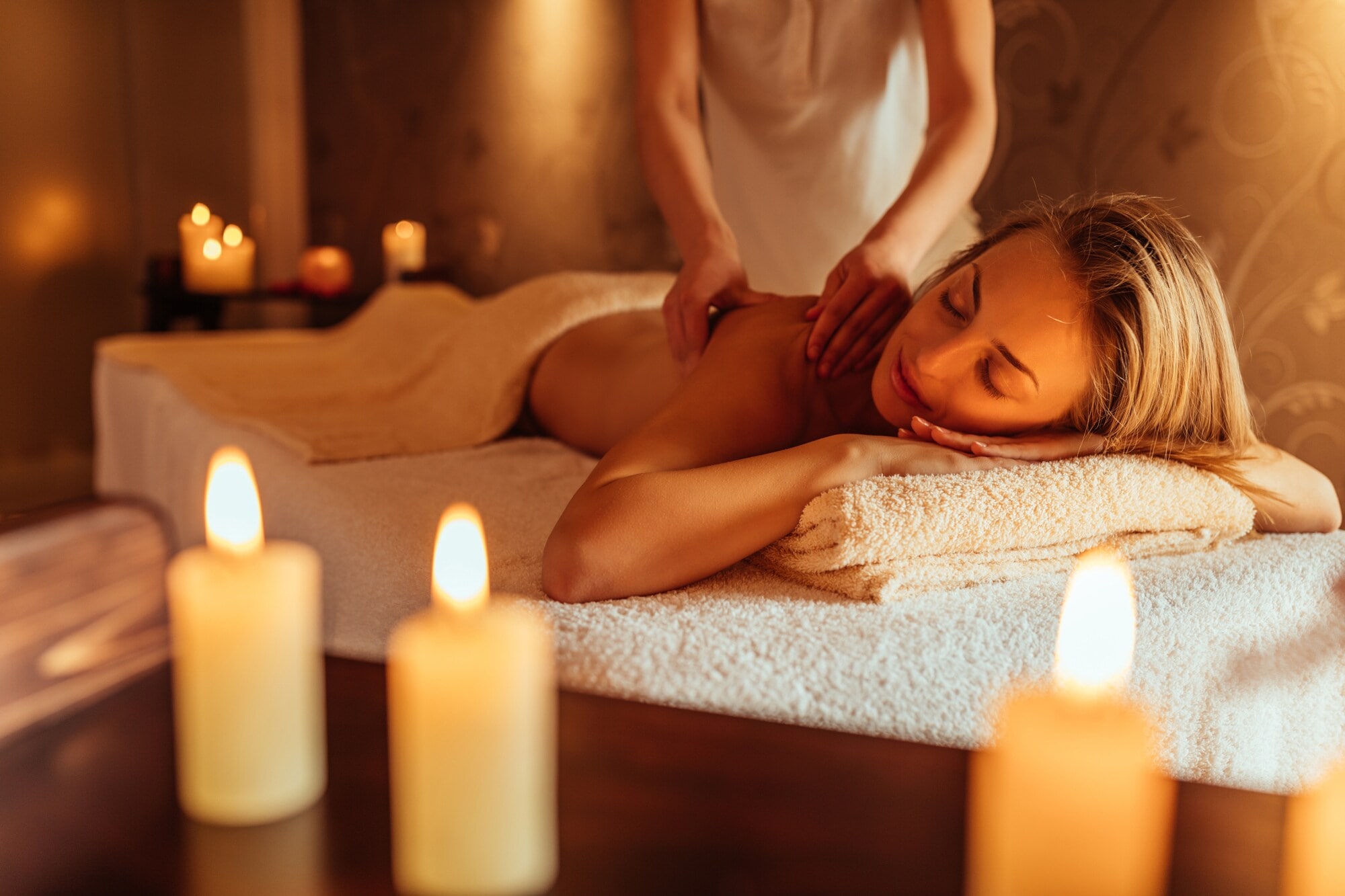 Eine junge Frau genießt bei Kerzenschein eine Rückenmassage in einem Wellness-Bereich Eine junge Frau genießt bei Kerzenschein eine Rückenmassage in einem Wellness-Bereich