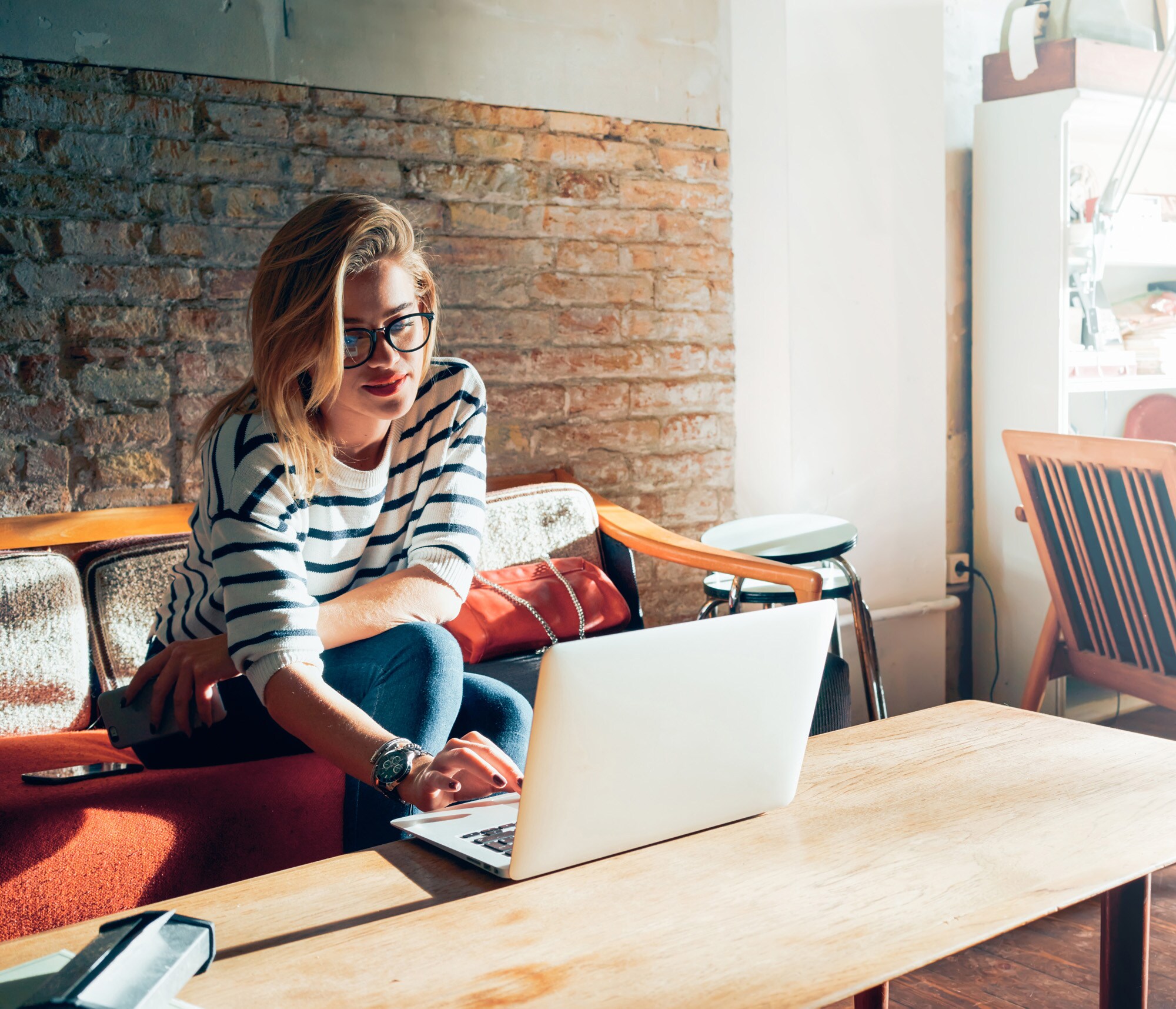 Eine junge Frau sitzt in einem Zimmer mit Vintage-Möbeln auf einem Sofa und arbeitet an ihrem Laptop