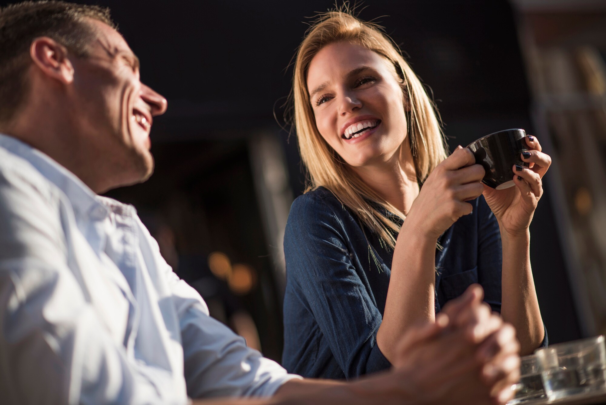 Ein Mann und eine Frau sitzen lachend nebeneinander, sie genießt eine Tasse Cappuccino Ein Mann und eine Frau sitzen lachend nebeneinander, sie genießt eine Tasse Cappuccino