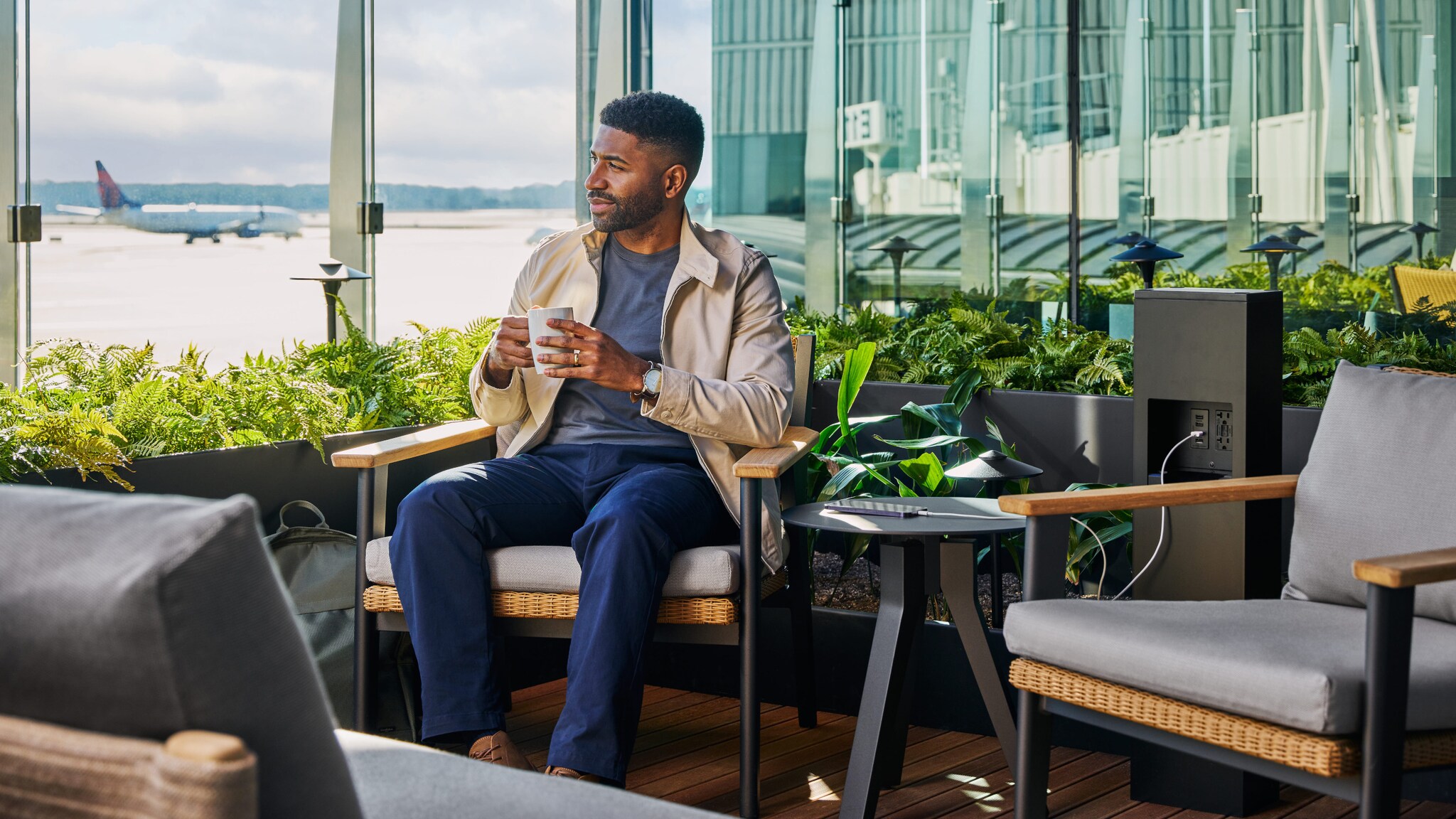 Ein Mann mit Kaffeetasse auf der Terrasse einer modernen Flughafenlounge mit Blick aufs Rollfeld. Ein Mann mit Kaffeetasse auf der Terrasse einer modernen Flughafenlounge mit Blick aufs Rollfeld.