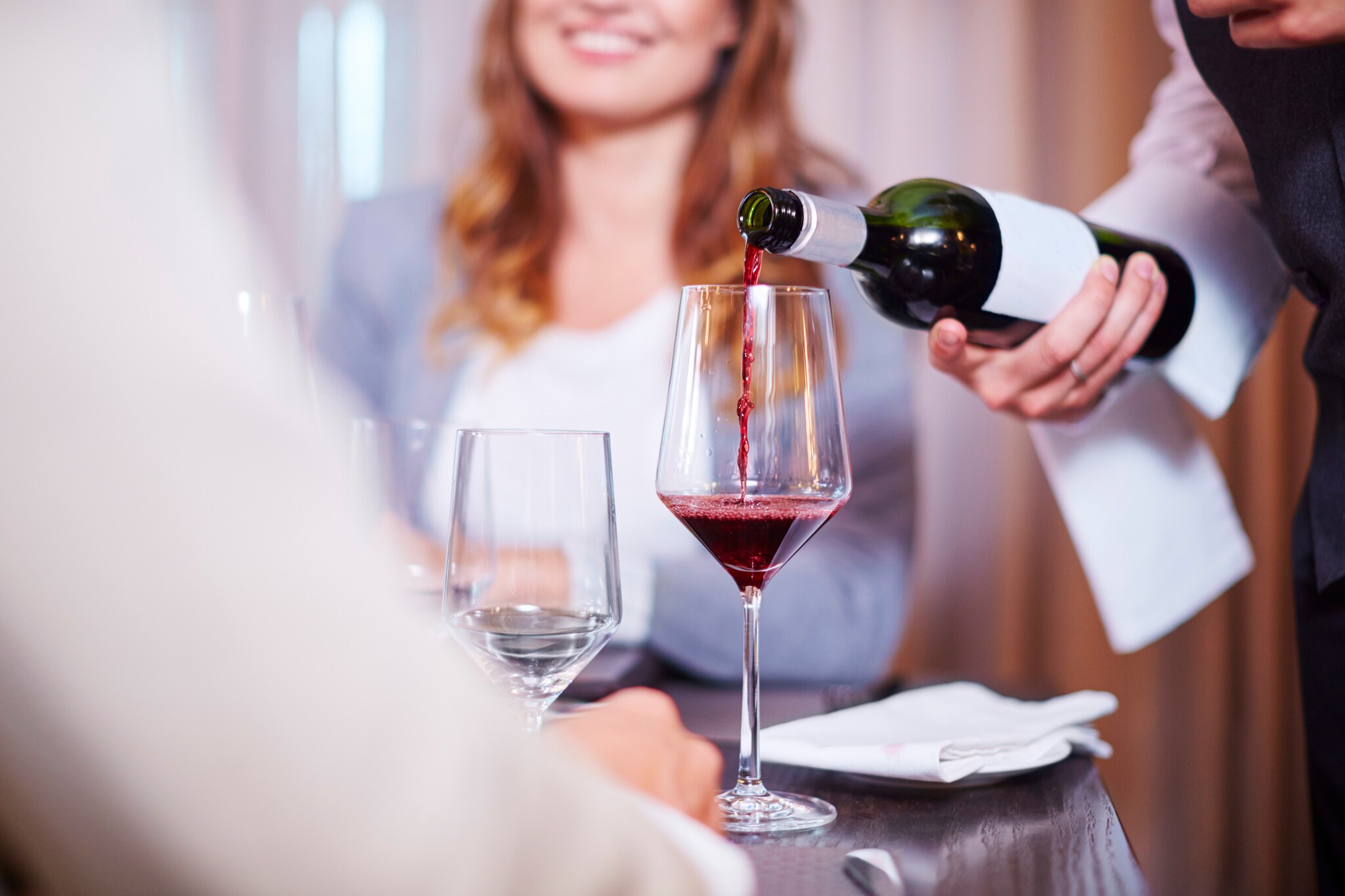 Ein Kellner gießt Rotwein in ein Glas an einem elegant gedeckten Tisch mit zwei Personen