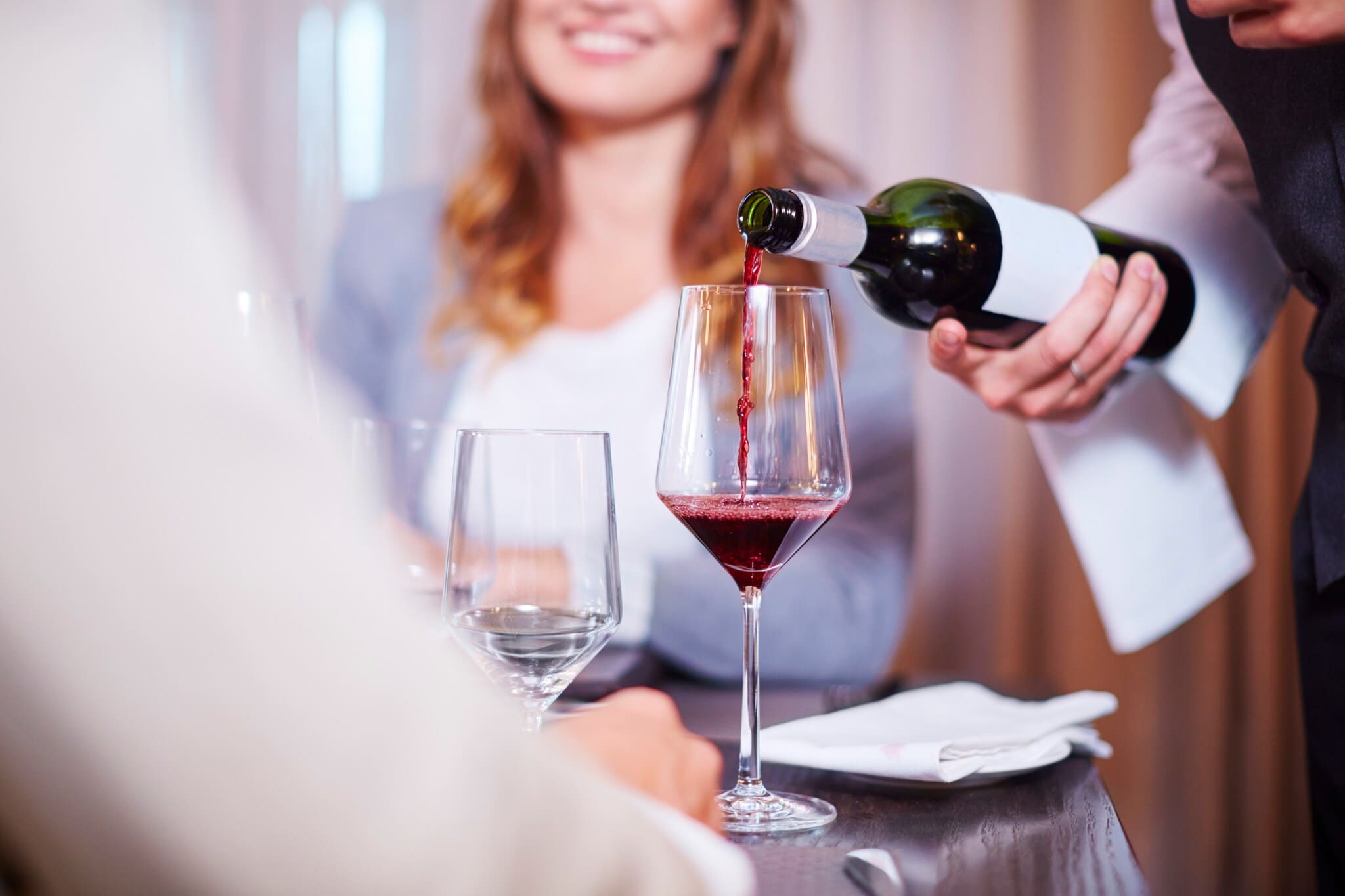 Ein Kellner gießt Rotwein in ein Glas an einem elegant gedeckten Tisch mit zwei Personen Ein Kellner gießt Rotwein in ein Glas an einem elegant gedeckten Tisch mit zwei Personen