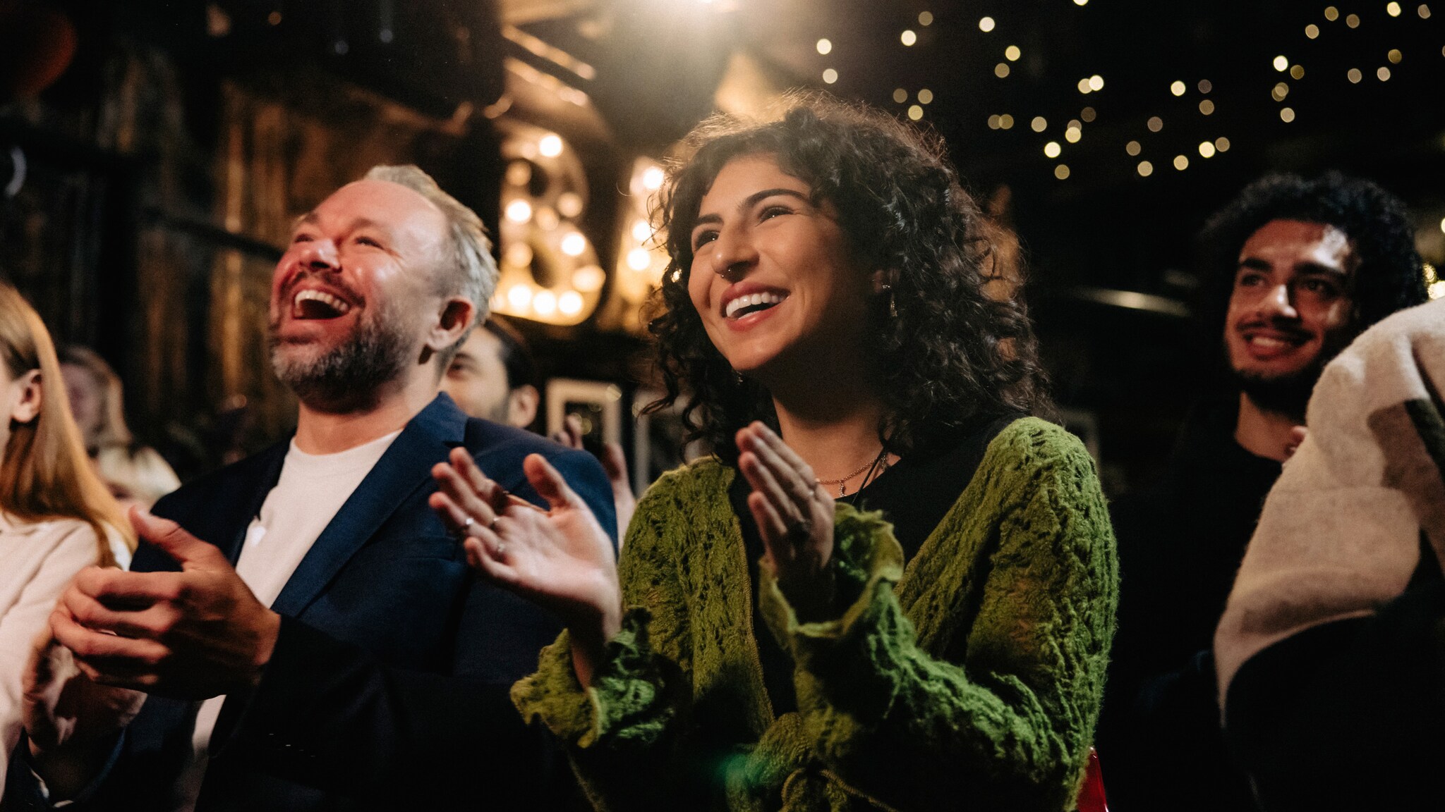 Nahaufnahme von einem lachenden und klatschenden Paar im Publikum bei einer Veranstaltung.