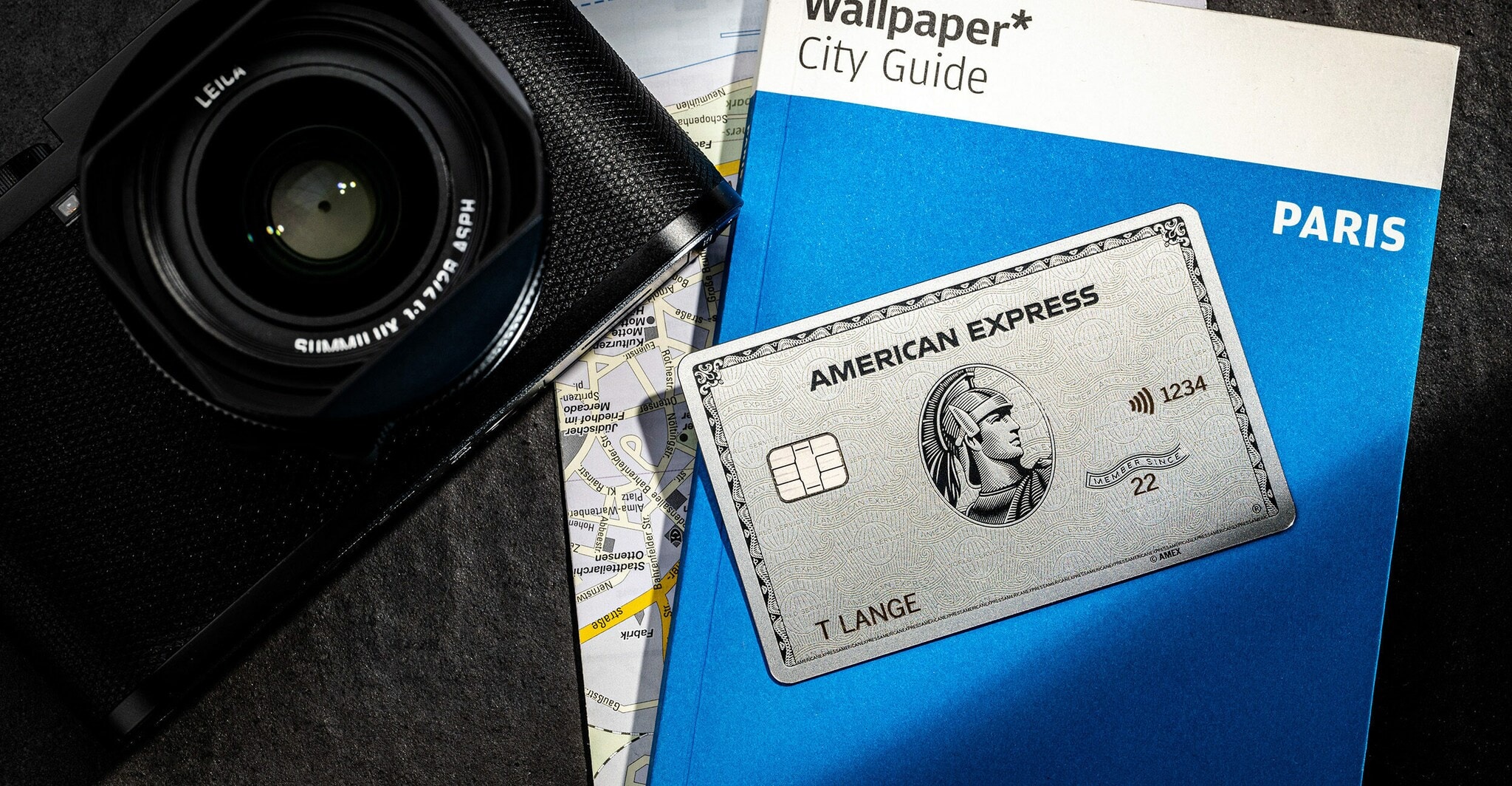 Eine American Express Platinum Card liegt auf einem blauen Reiseführer neben einer edlen, schwarzen Kamera Eine American Express Platinum Card liegt auf einem blauen Reiseführer neben einer edlen, schwarzen Kamera