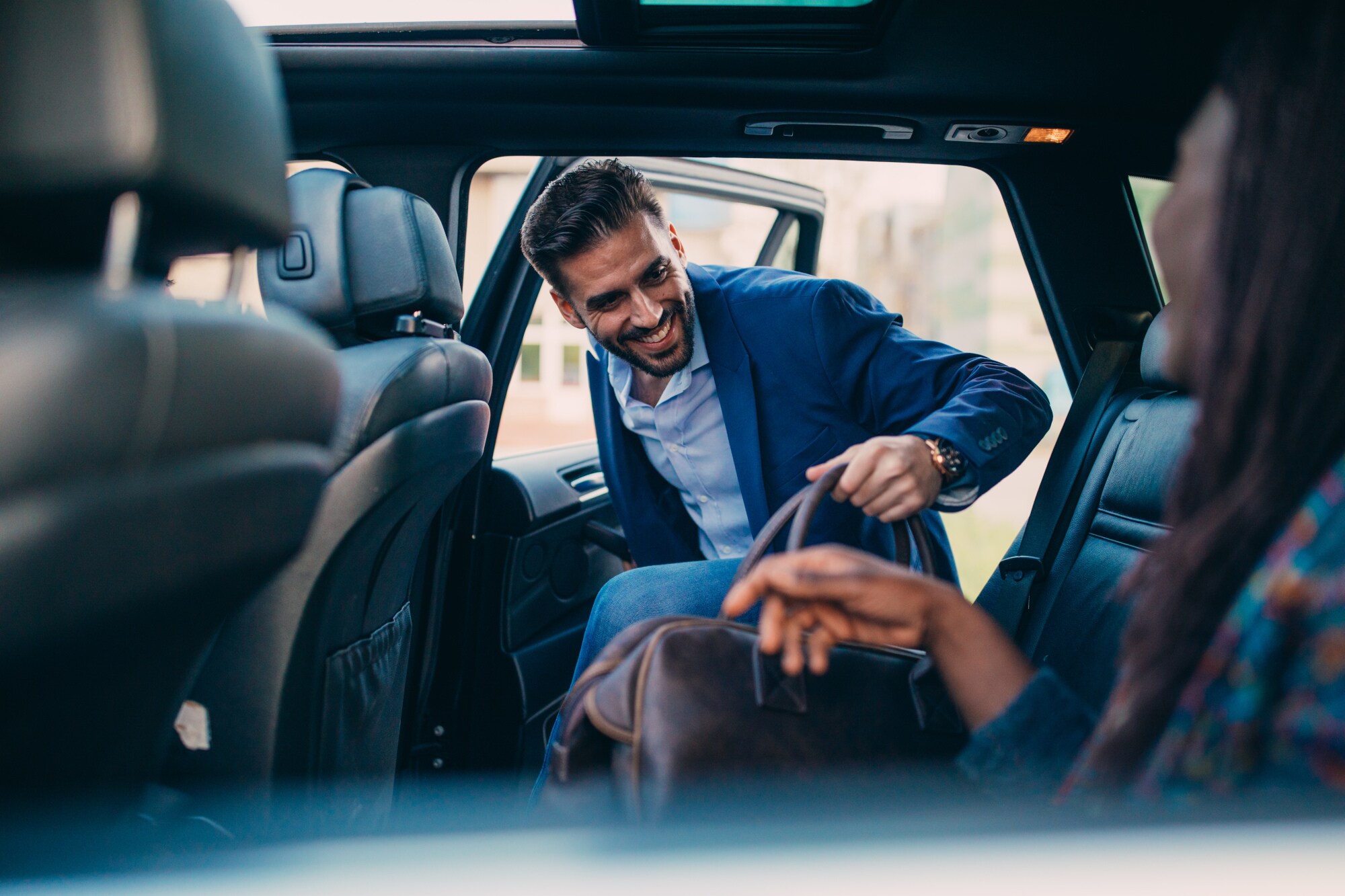 Ein elegant gekleideter Mann steigt mit einer Reisetasche auf den Rücksitz eines Autos ein Ein elegant gekleideter Mann steigt mit einer Reisetasche auf den Rücksitz eines Autos ein