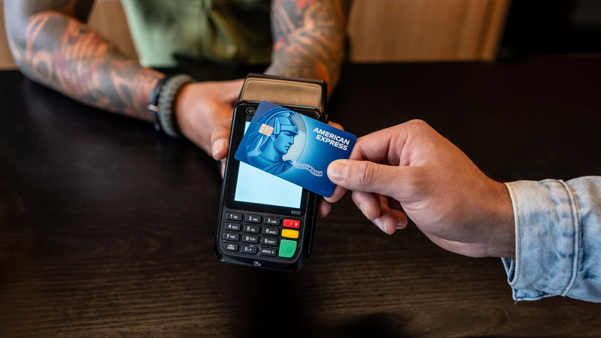 Kontaktlose Zahlung mit einer blauen American Express Kreditkarte an einem Kartenlesegerät.