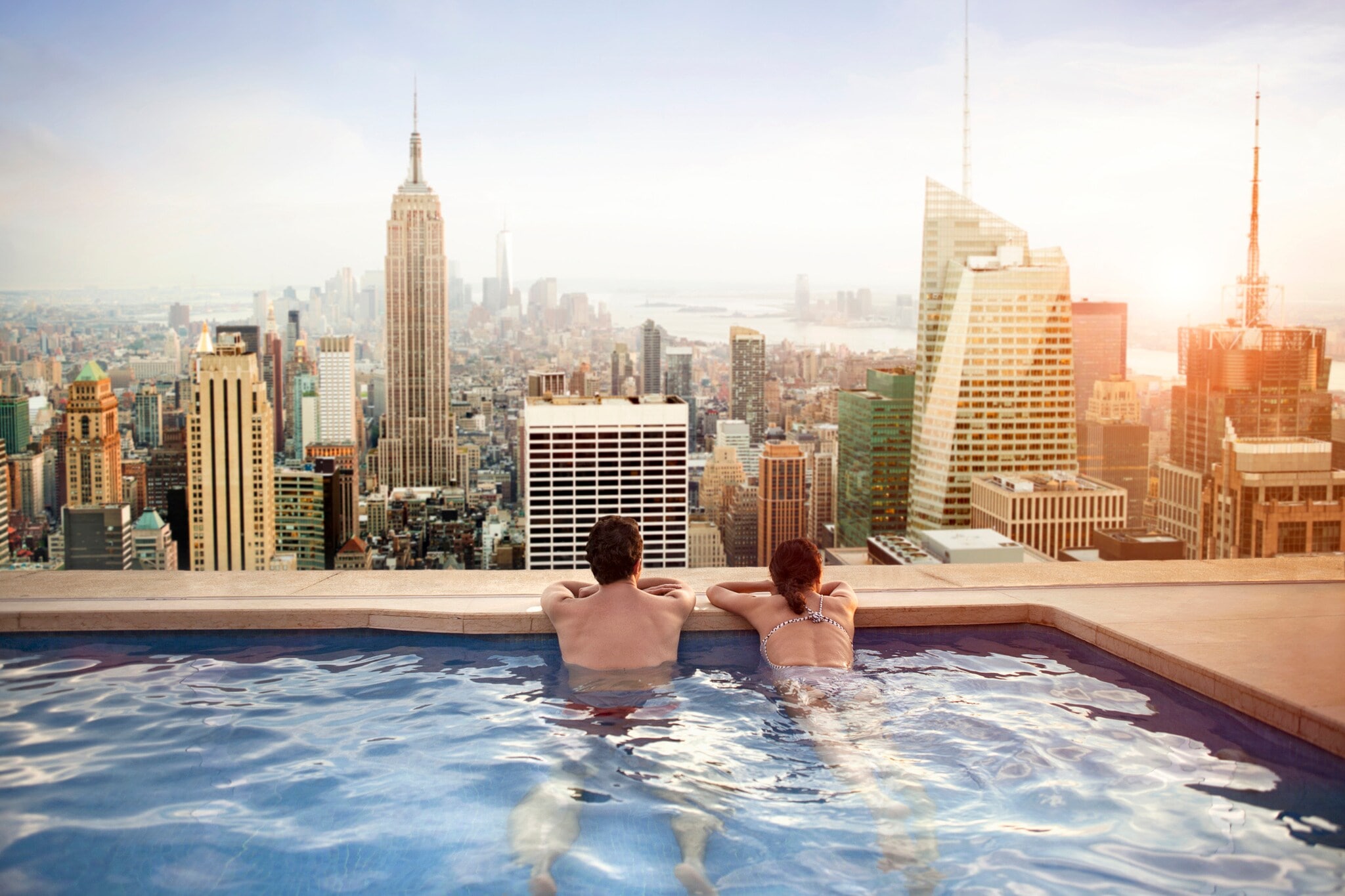Rückansicht eines Paares in einem Rooftop-Pool, das auf die Skyline von Manhattan blickt Rückansicht eines Paares in einem Rooftop-Pool, das auf die Skyline von Manhattan blickt
