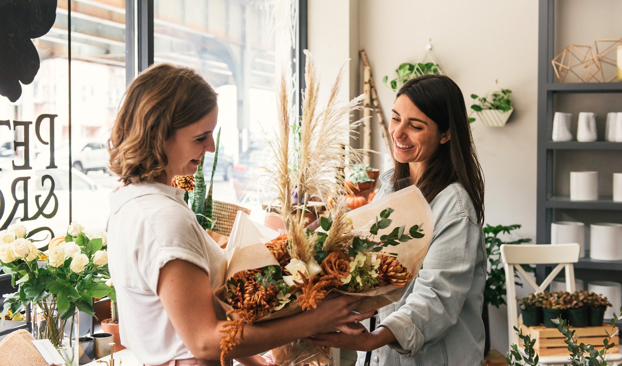 Eine Kundin nimmt in einem Blumengeschäft einen Blumenstrauß von der Verkäuferin entgegen Eine Kundin nimmt in einem Blumengeschäft einen Blumenstrauß von der Verkäuferin entgegen