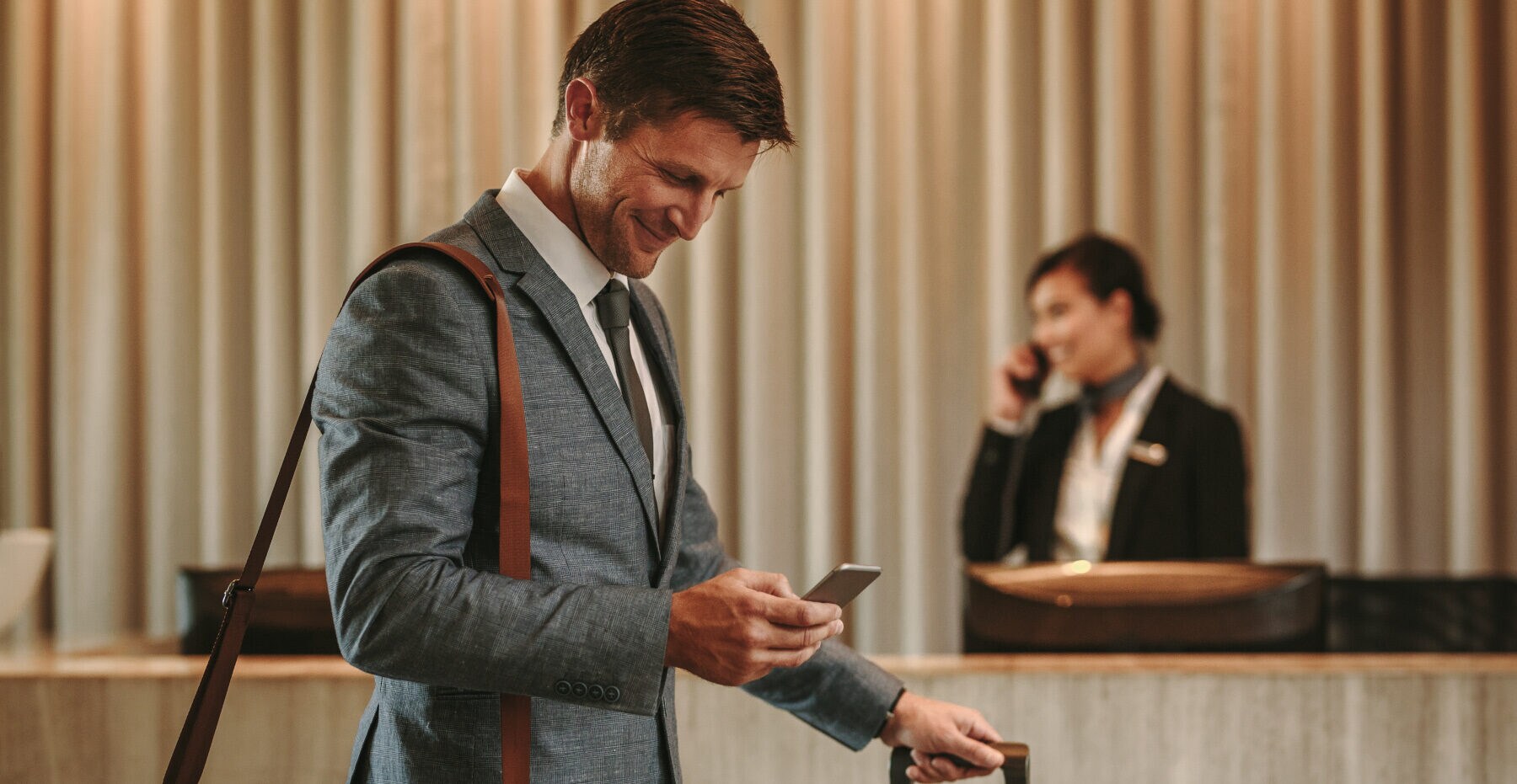 Ein Geschäftsmann schaut lächelnd auf sein Smartphone in einer Hotellobby Ein Geschäftsmann schaut lächelnd auf sein Smartphone in einer Hotellobby
