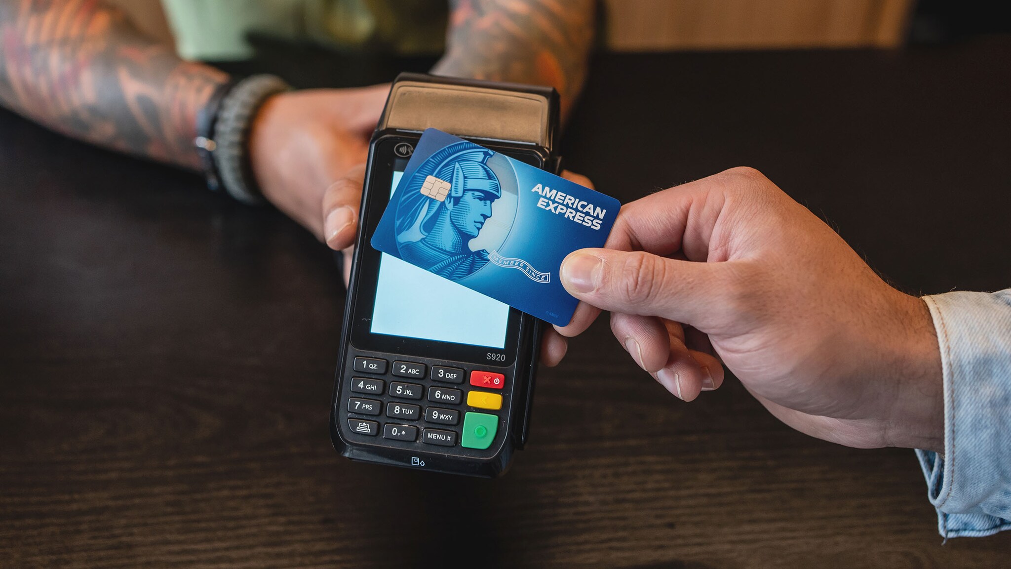 Kontaktlose Zahlung mit einer blauen Kreditkarte von American Express an einem Kartenlesegerät auf einer Theke. Kontaktlose Zahlung mit einer blauen Kreditkarte von American Express an einem Kartenlesegerät auf einer Theke.