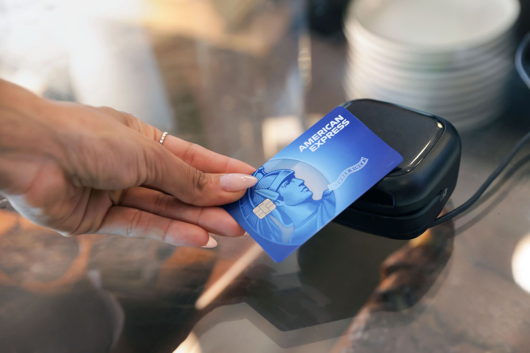 Kontaktlose Zahlung mit einer blauen American Express Kreditkarte an einem Kartenlesegerät.