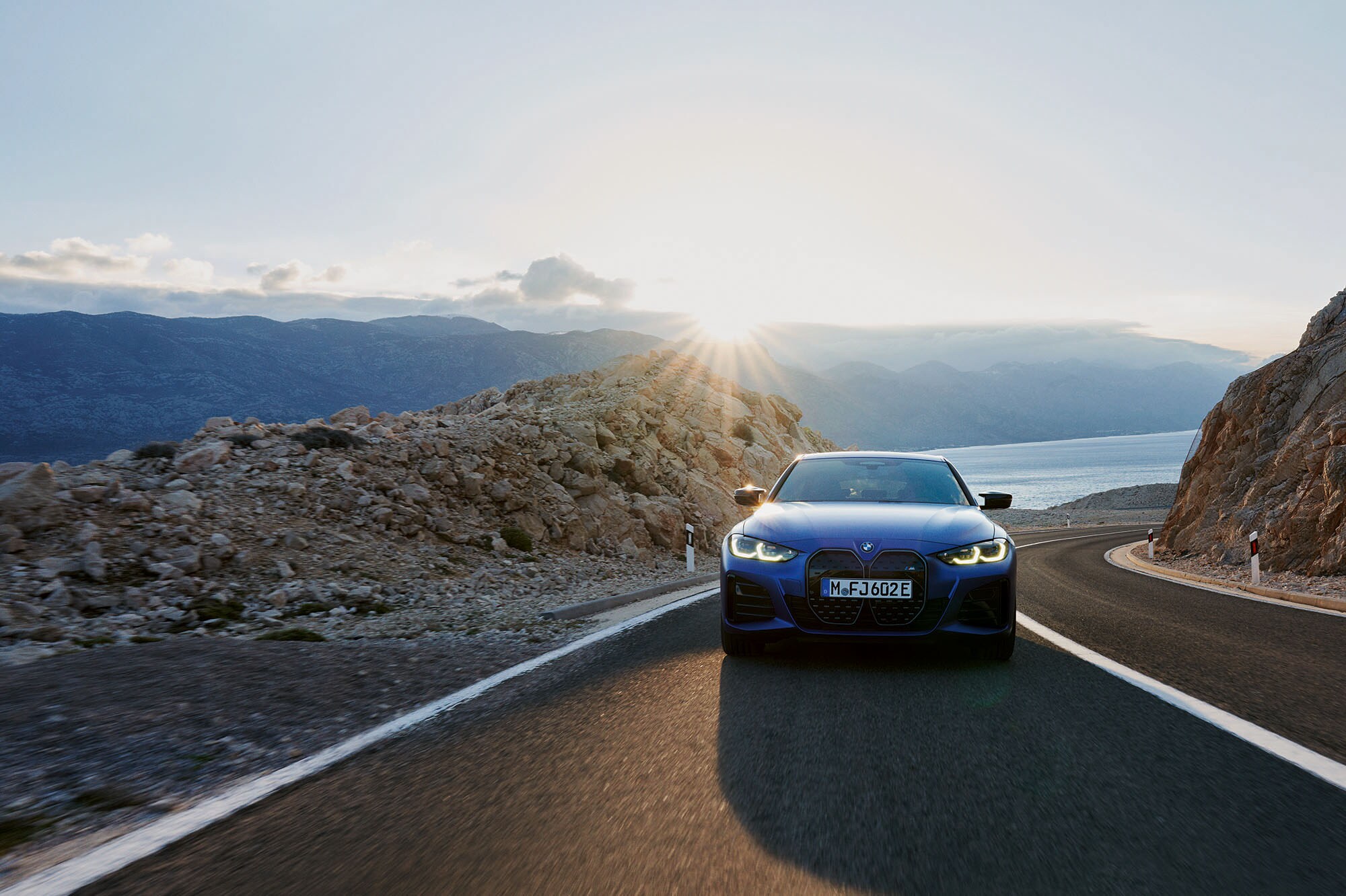 Vorderansicht eines blauen Autos der Marke BMW, das auf einer gebirgigen Küstenstraße fährt