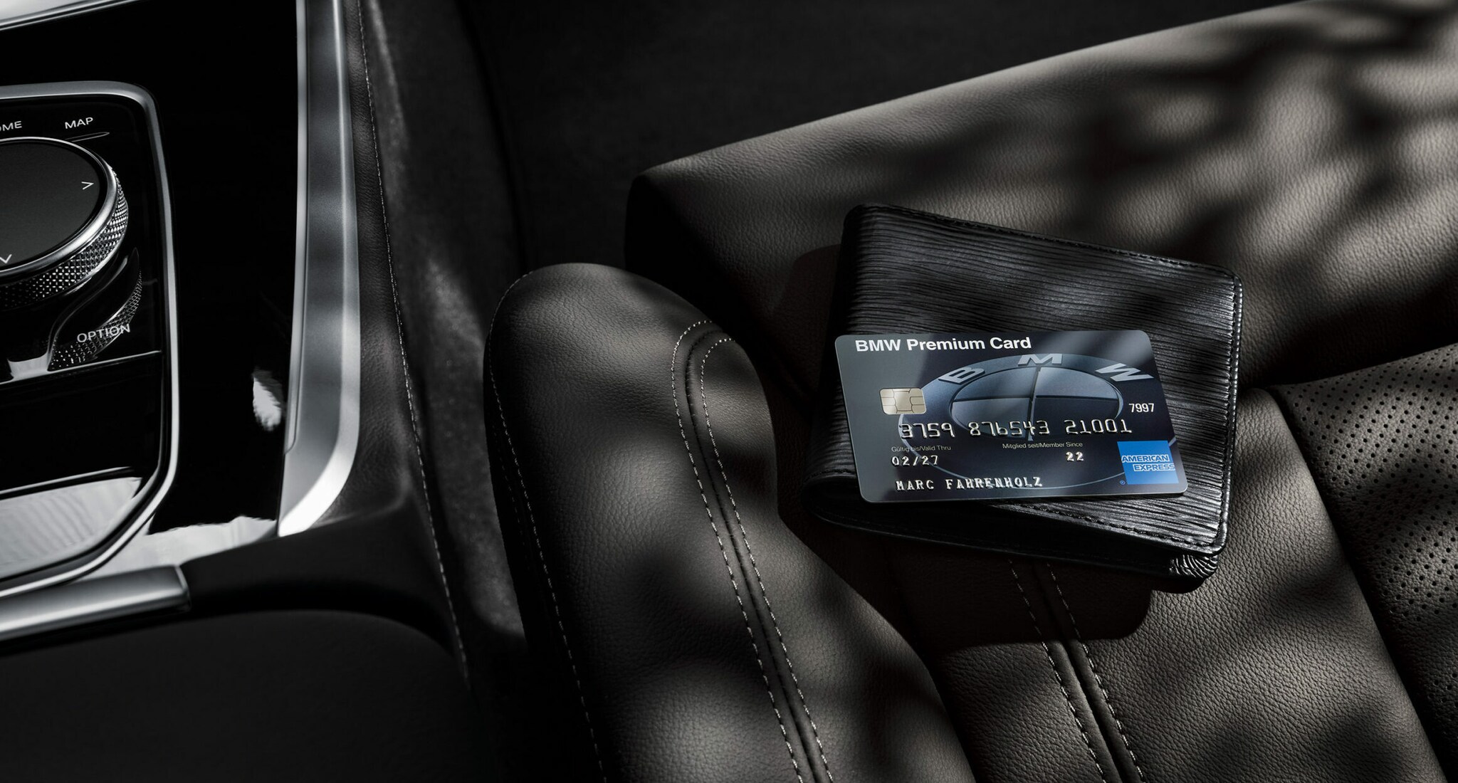 Eine schwarze BMW Premium Card von American Express liegt auf einem schwarzen Portemonnaie auf einem schwarzen Autositz aus Leder