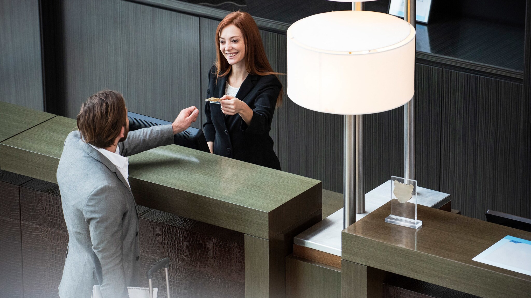 Eine Person gibt einer anderen Person über einen Tresen hinweg eine Kreditkarte an einer Hotelrezeption. Eine Person gibt einer anderen Person über einen Tresen hinweg eine Kreditkarte an einer Hotelrezeption.