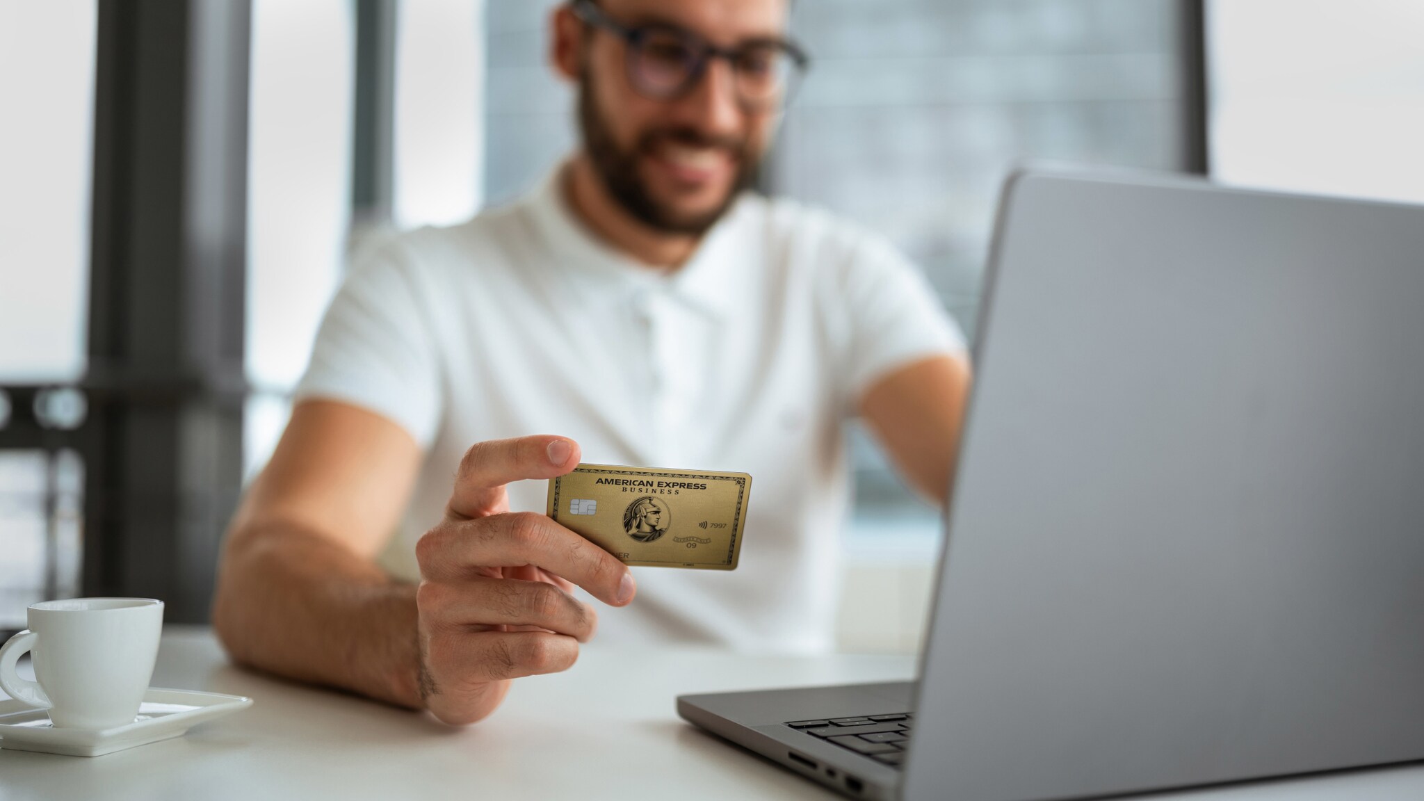 Eine Person vor einem Laptop hält eine Business Gold Card von American Express in der Hand. Eine Person vor einem Laptop hält eine Business Gold Card von American Express in der Hand.