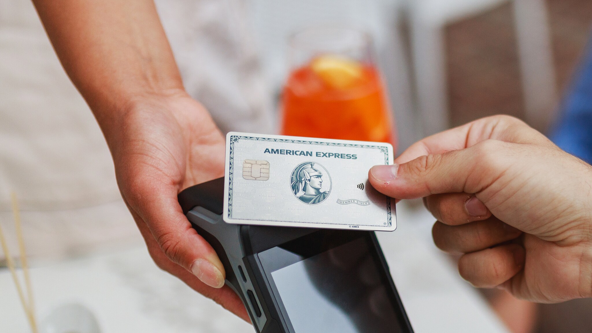 Kontaktlose Zahlung mit einer silbernen Platinum Kreditkarte von American Express an einem Kartenlesegerät in einem Restaurant.