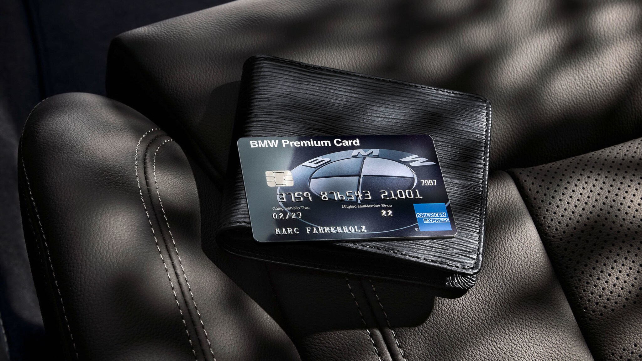 Eine schwarze BMW Premium Card von American Express legt auf einem schwarzen Portemonnaie auf einem Autositz aus schwarzem Leder.