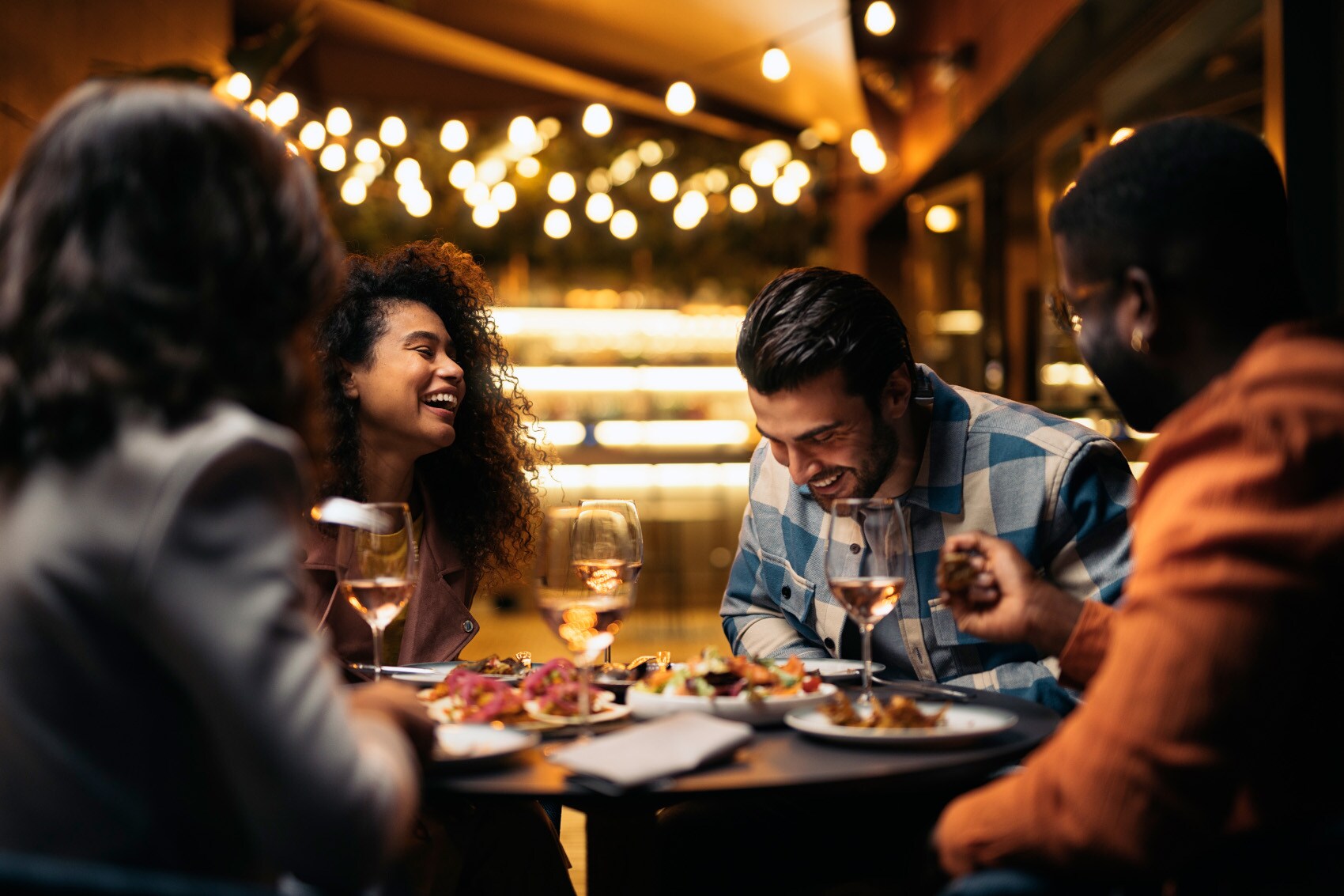 Vier junge Personen sitzen gut gelaunt beim Abendessen an einem runden Tisch in einem gehobenen Restaurant.