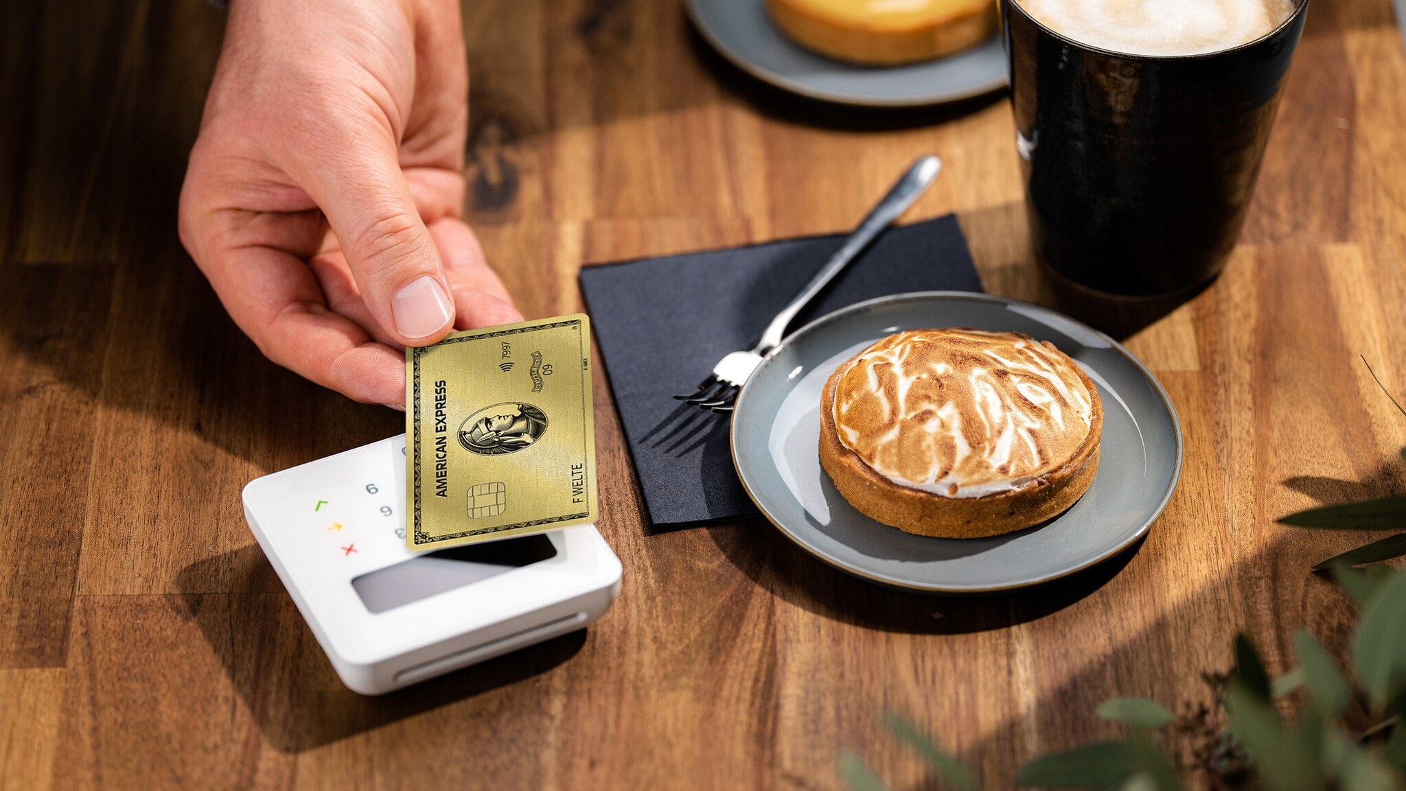 Kontaktlose Zahlung an einem Kartenlesegerät mit einer American Express Gold Card in einem Café. Kontaktlose Zahlung an einem Kartenlesegerät mit einer American Express Gold Card in einem Café.
