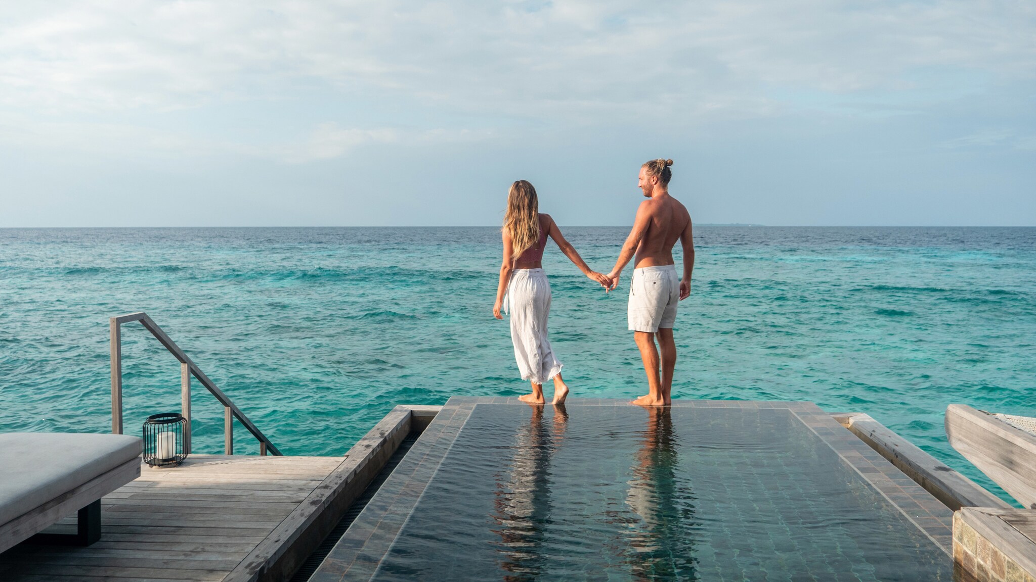 Rückansicht eines Paares in Sommerkleidung an einem luxuriösen Pool am Meer.