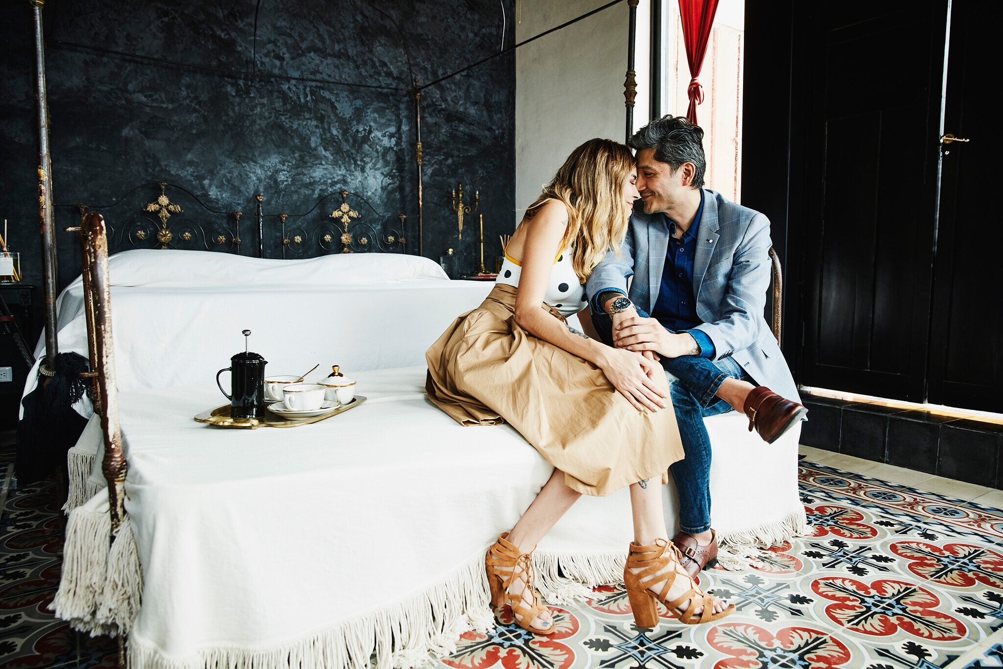 Ein Paar sitzt aneinander gekuschelt auf einem großen Bett in einem Hotelzimmer mit orientalischem Dekor.