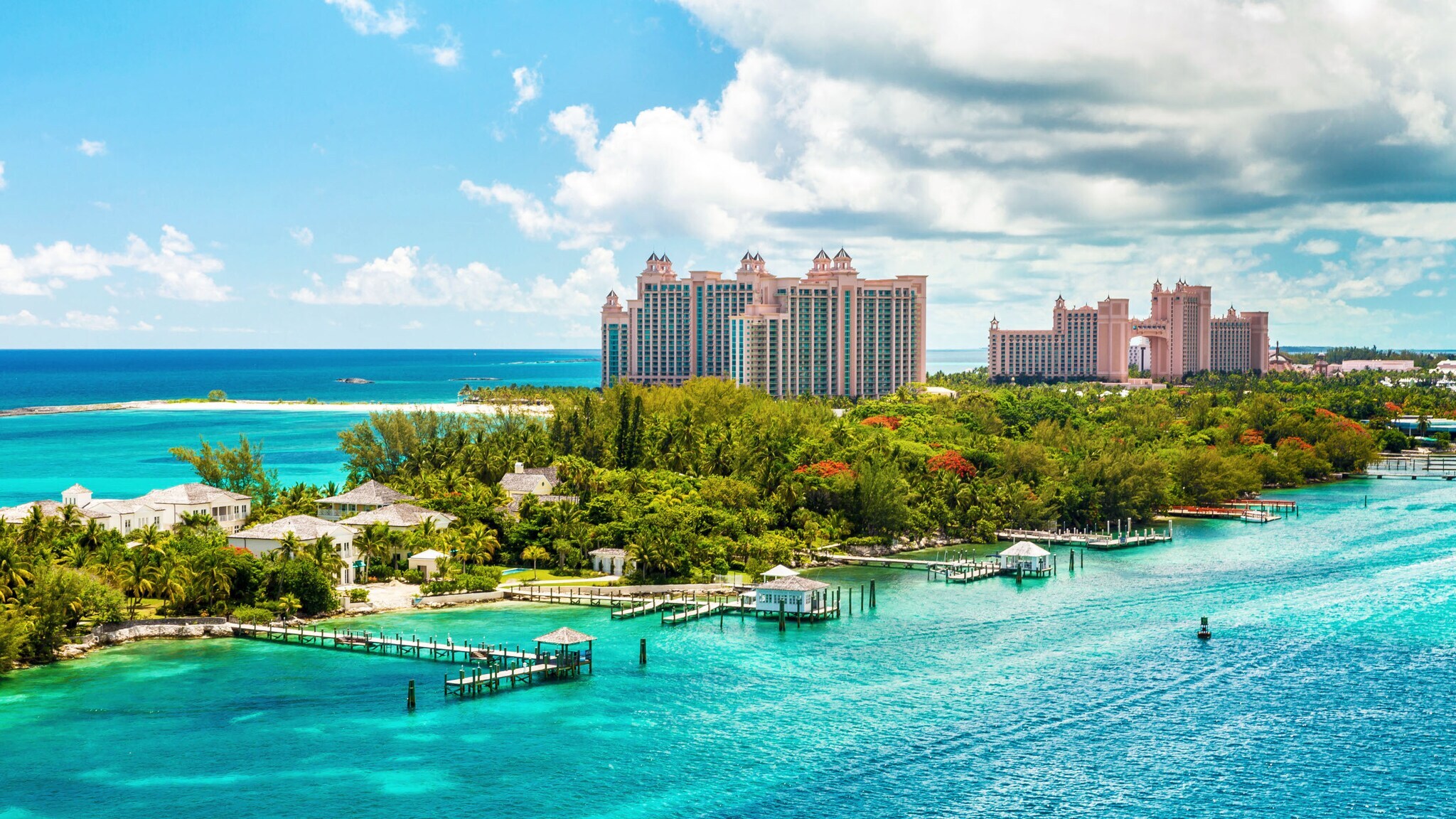 Hotelkomplex aus rosafarbenen Hochhäusern mit Türmen auf einer Insel mit tropischer Vegetation und Holzstegen im türkisblauen Meer.