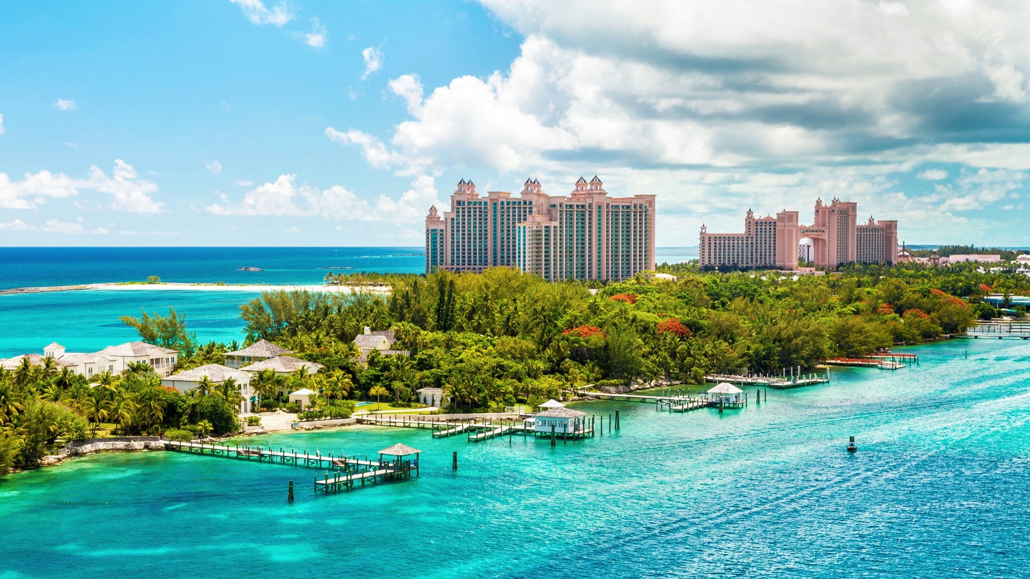 Hotelkomplex aus rosafarbenen Hochhäusern mit Türmen auf einer Insel mit tropischer Vegetation und Holzstegen im türkisblauen Meer. Hotelkomplex aus rosafarbenen Hochhäusern mit Türmen auf einer Insel mit tropischer Vegetation und Holzstegen im türkisblauen Meer.