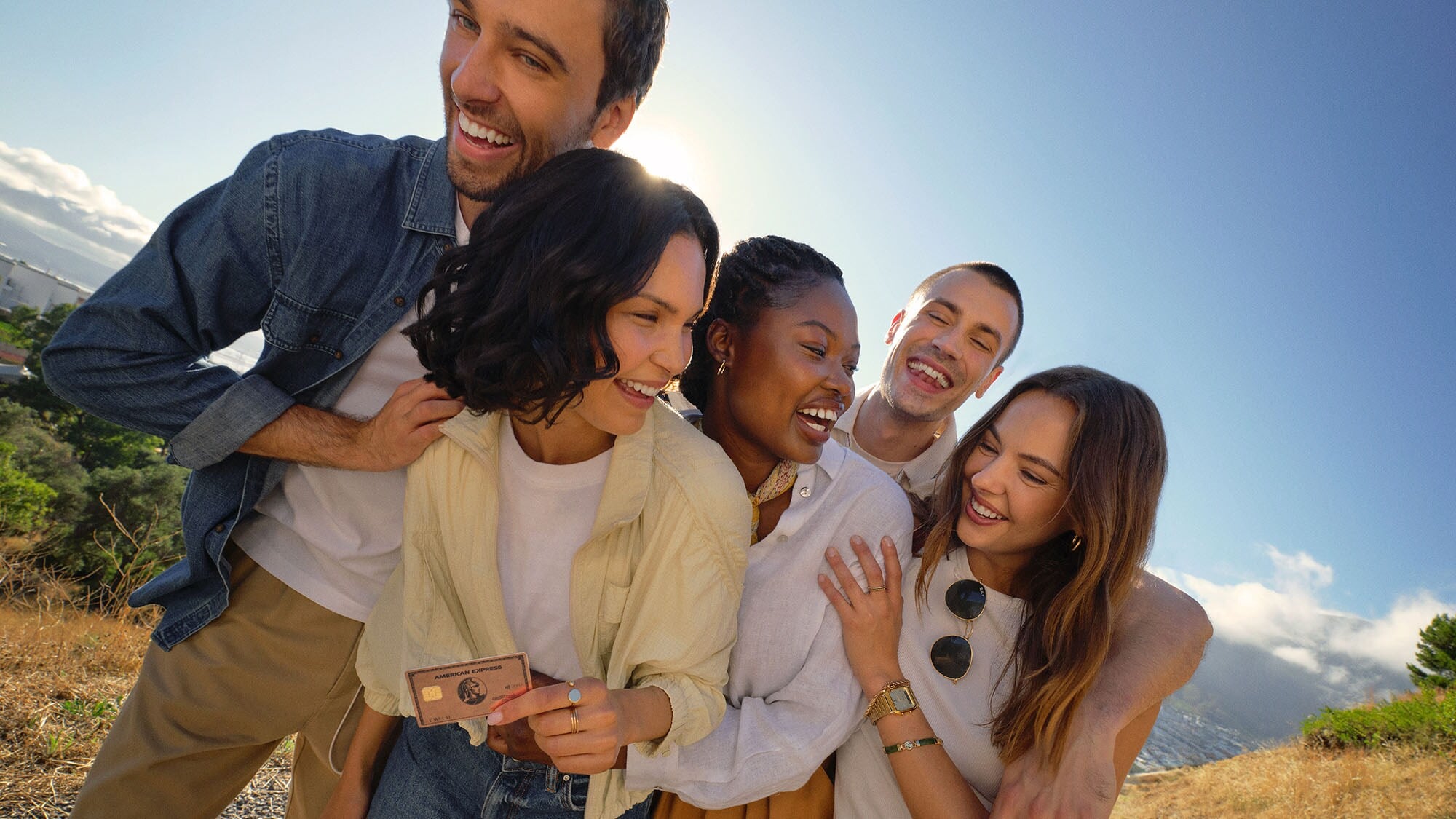 Drei Frauen und zwei Männer liegen sich lachend in den Armen und stehen bei strahlendem Sonnenschein auf einem Weg in der Natur. Drei Frauen und zwei Männer liegen sich lachend in den Armen und stehen bei strahlendem Sonnenschein auf einem Weg in der Natur.