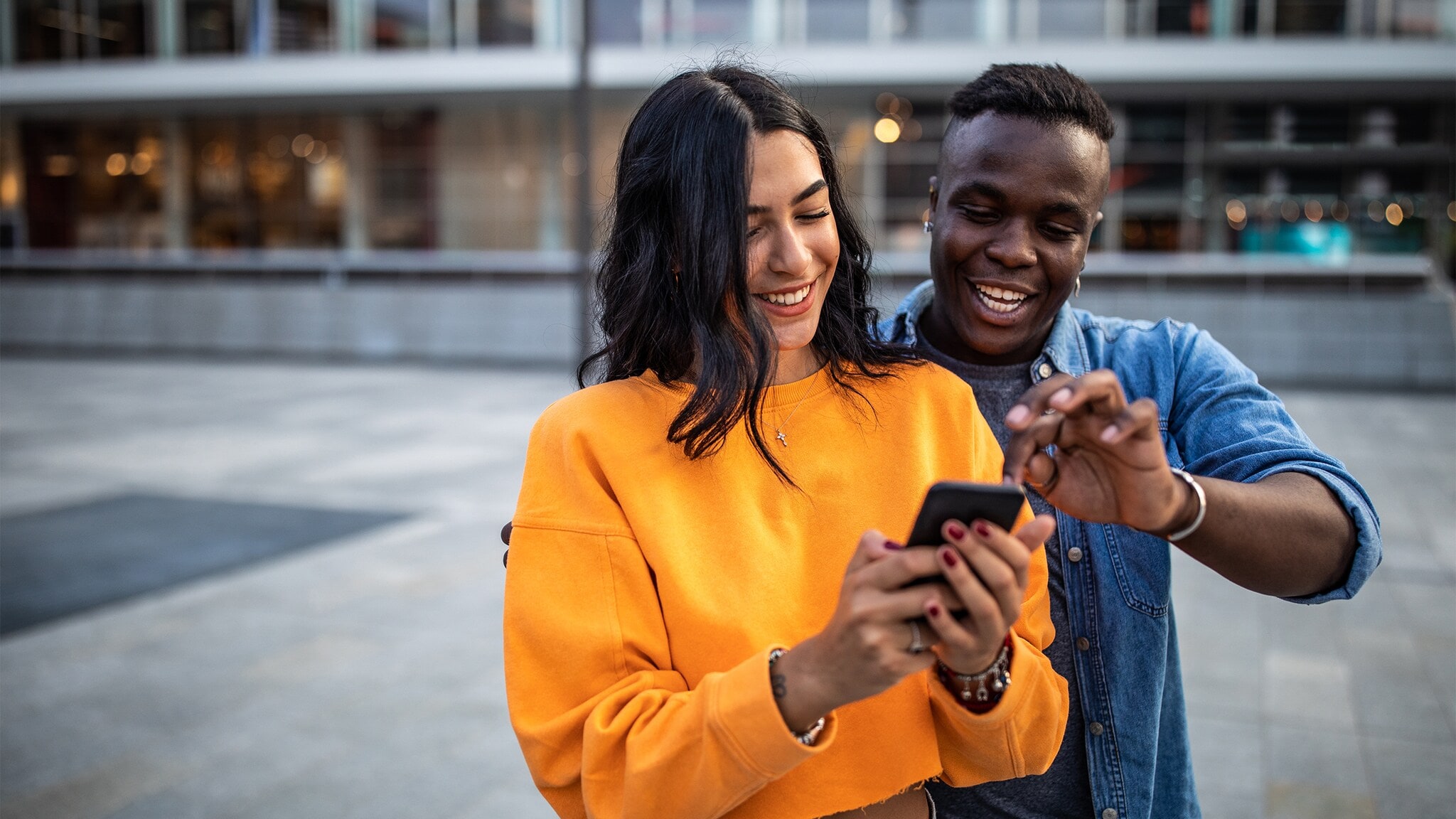 Ein junges Paar steht auf einer Straße und schaut gemeinsam auf ein Smartphone. Ein junges Paar steht auf einer Straße und schaut gemeinsam auf ein Smartphone.